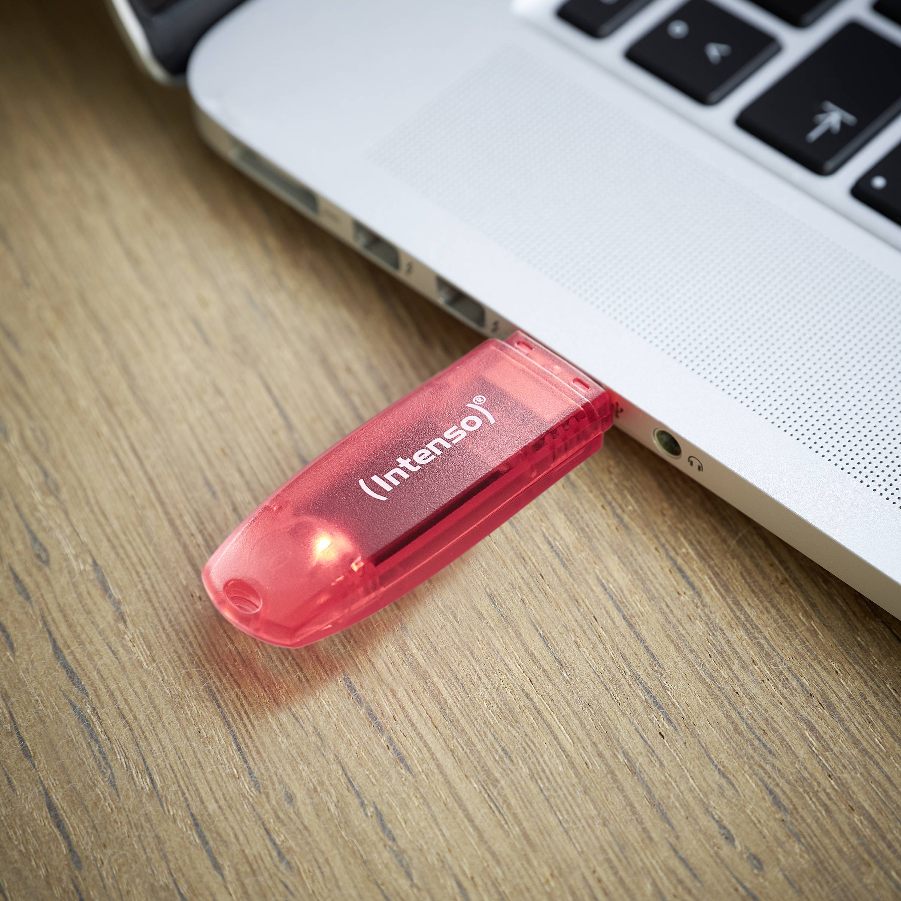 Ein roter USB-Stick mit der Aufschrift 'Intenso' steckt in einem Laptop, der auf einem Holztisch steht. Der Stick leuchtet rot.