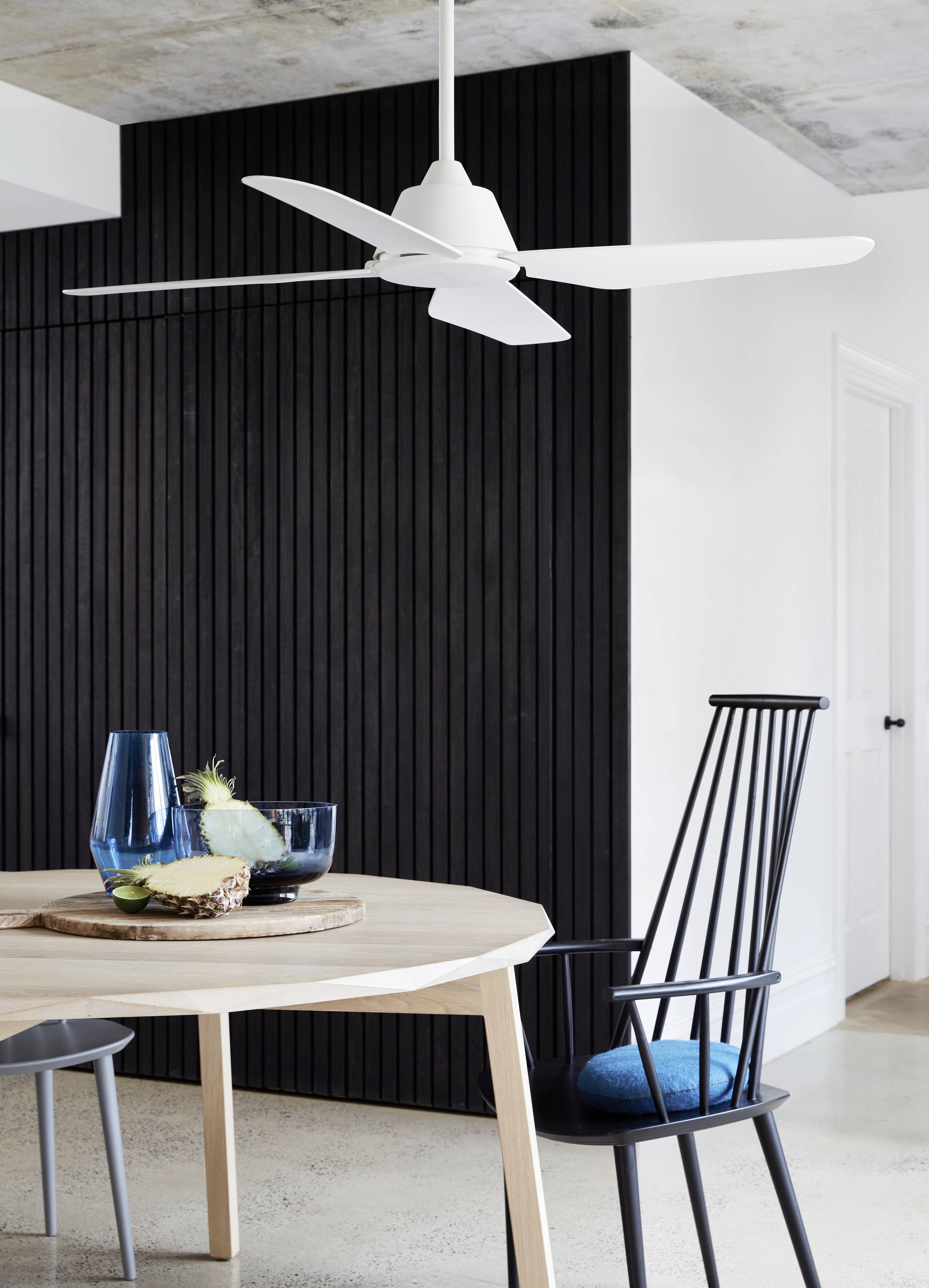 Esszimmer mit hellem Holztisch, schwarzem Stuhl und blauem Kissen. Auf dem Tisch steht ein Tablett mit blauen Gläsern und Ananas.