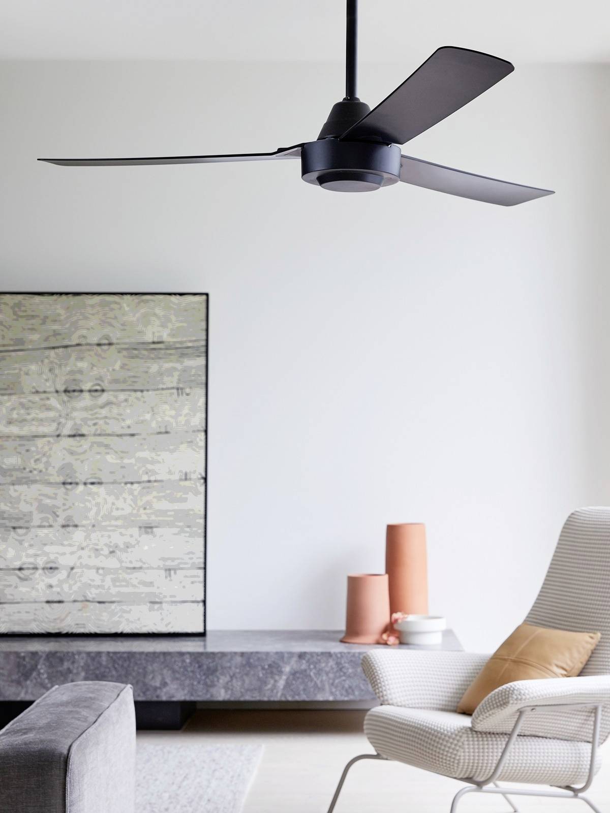 Ein Wohnzimmer mit modernem Deckenventilator, einem grauen Sofa, einem weißen Sessel mit Kissen und zwei orangefarbenen Vasen.