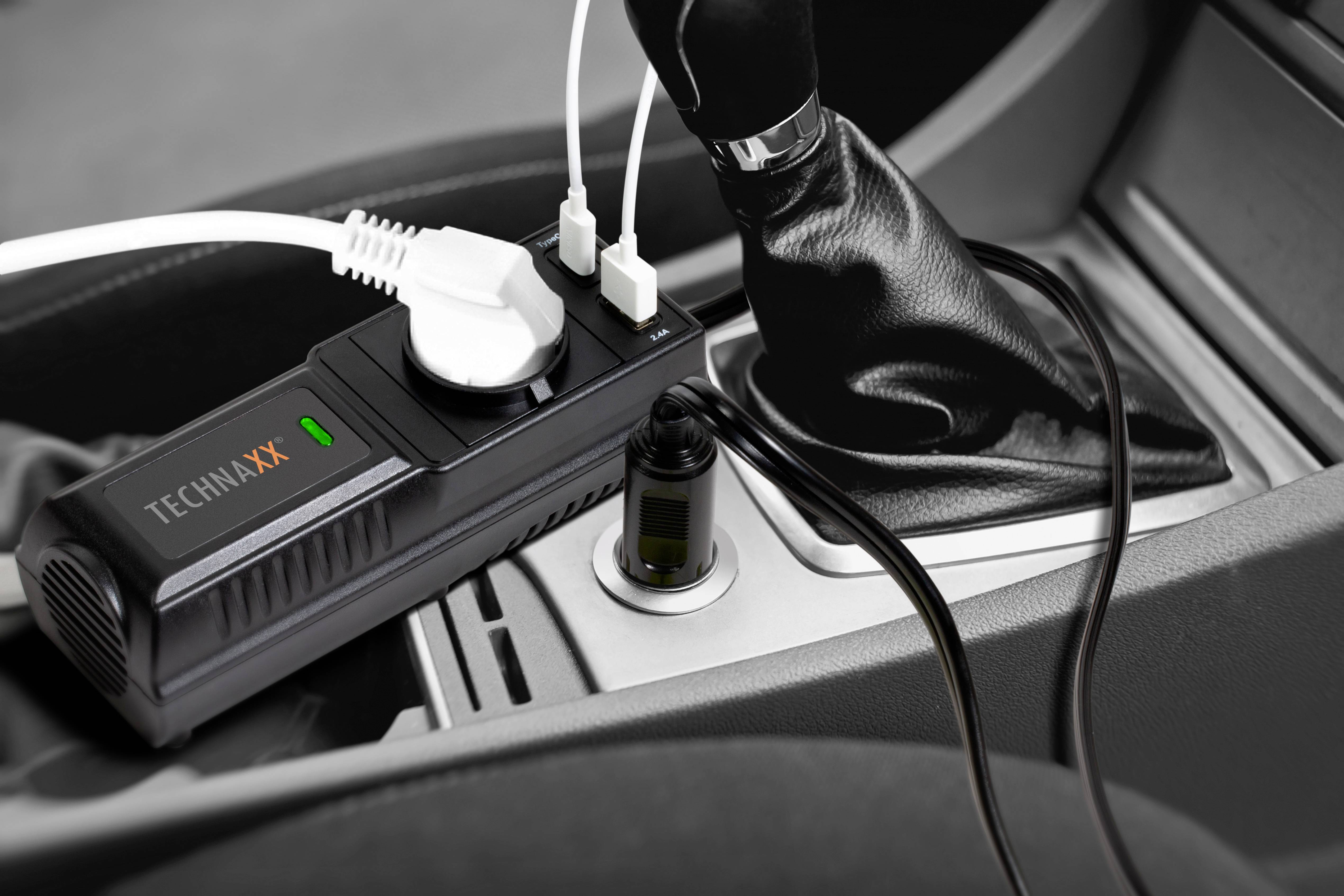 Ein Spannungswandler im Auto lädt zwei Geräte über USB und ein Gerät über ein Steckdosenkabel auf. Der Adapter ist neben dem Schalthebel platziert.