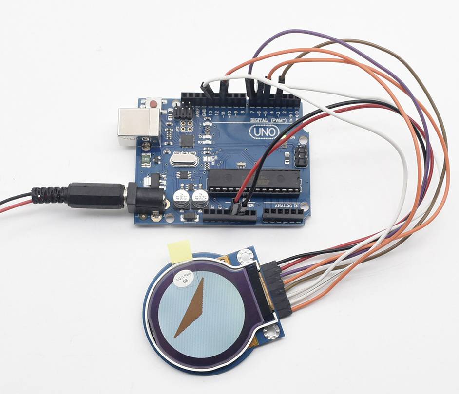Mikrocontrollerplatine mit mehreren Kabeln und einem angeschlossenen runden Display, das einen Kompasspfeil zeigt.