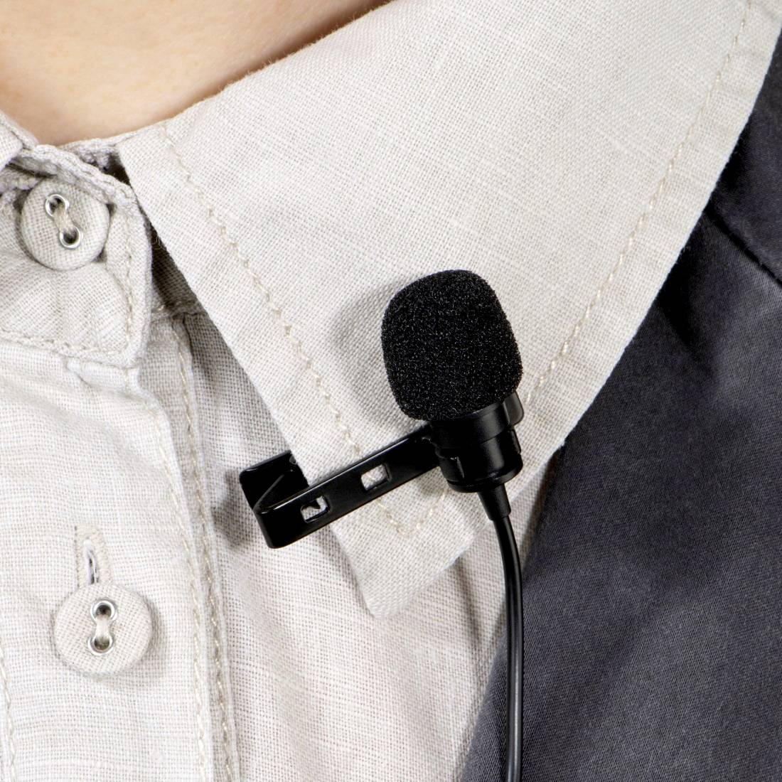 Eine Person trägt ein Mikrofon, das an ihrem Hemdkragen befestigt ist. Das Mikrofon ist schwarz und klein, ideal für Aufnahmen.