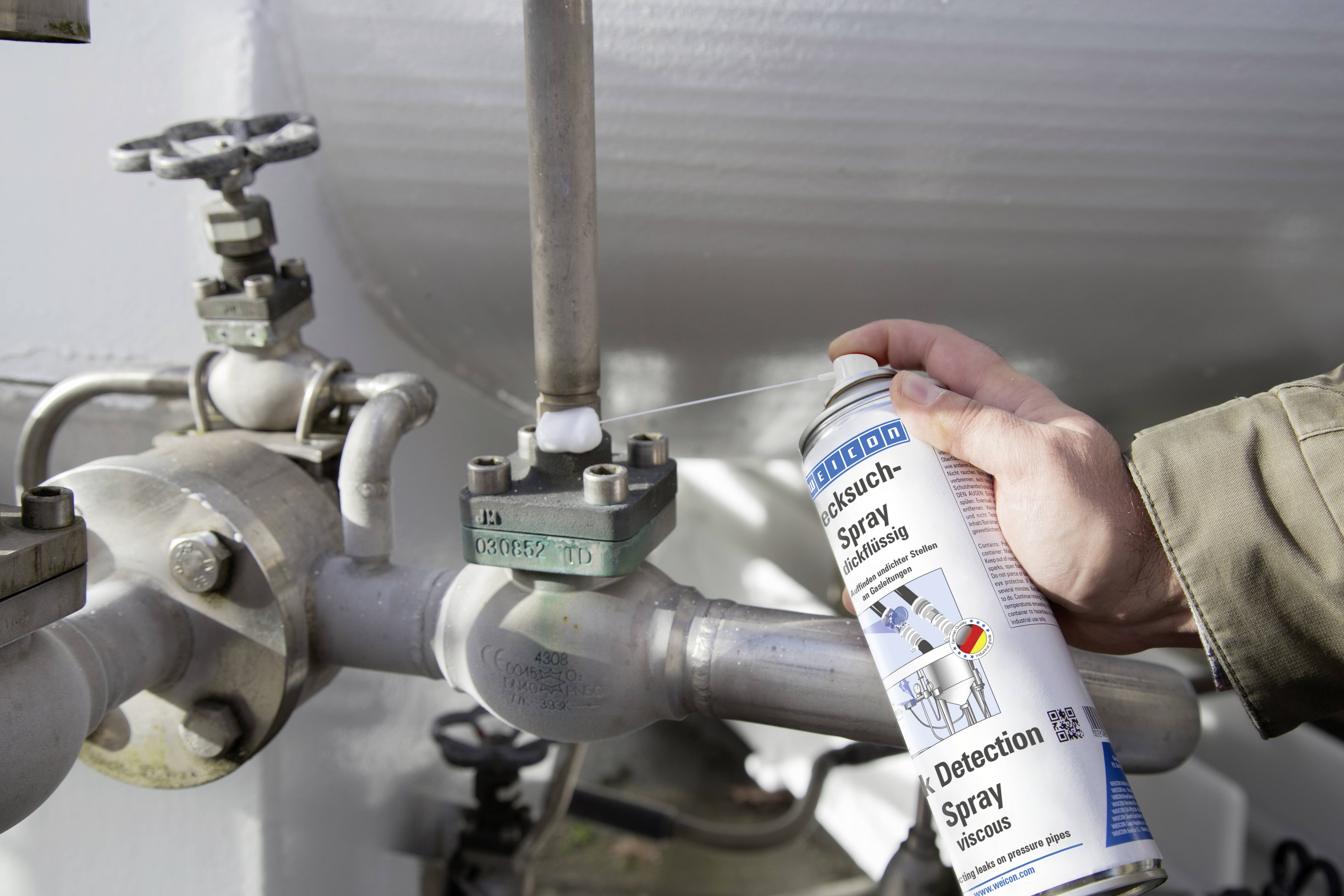 Eine Person benutzt ein Lecksuchspray an einem Rohrsystem, um eventuelle Gas- oder Flüssigkeitsaustritte zu überprüfen.
