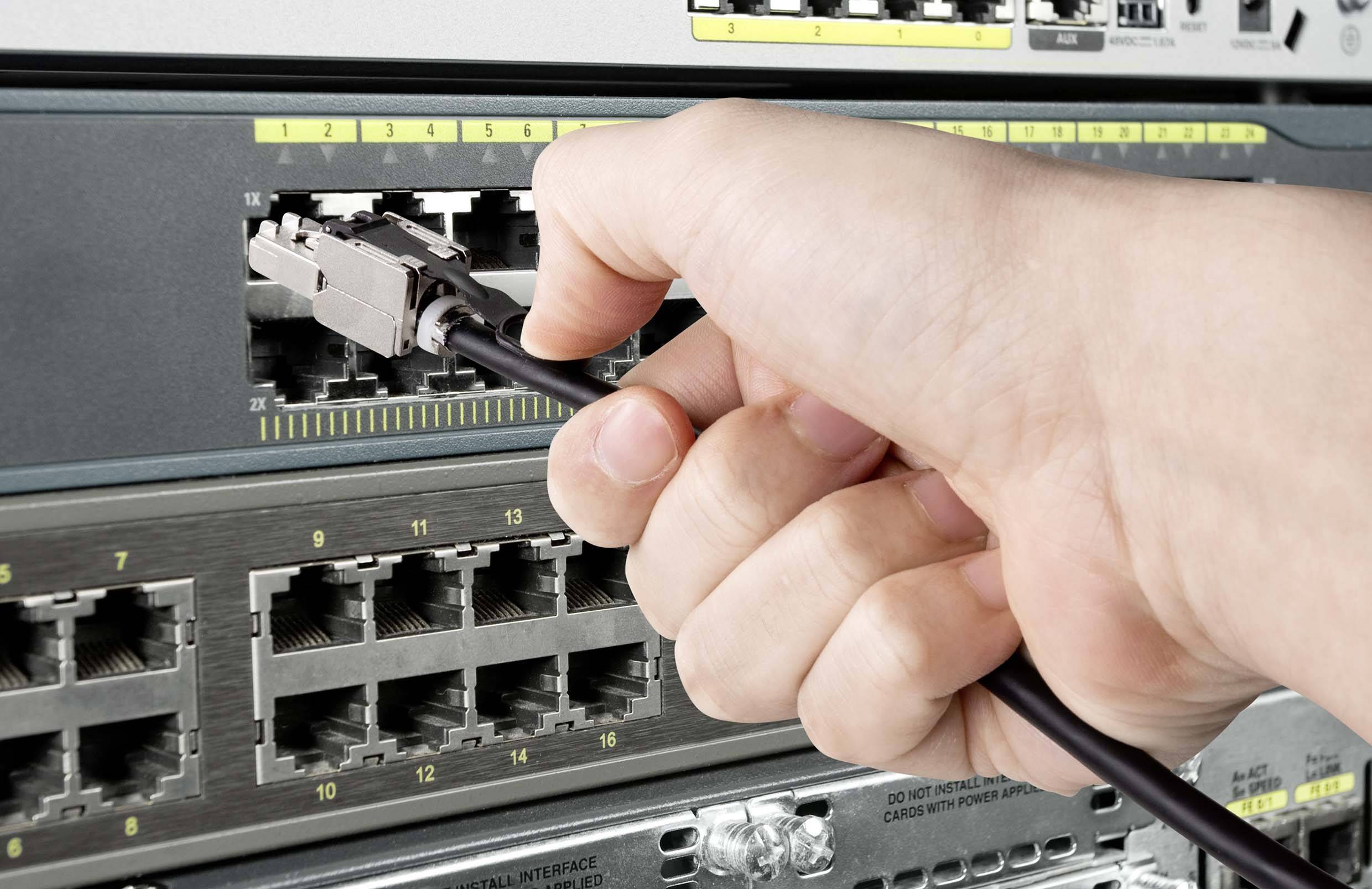 Eine Hand steckt ein Kabel in einen Netzwerk-Switch, was auf eine Netzwerkverbindung oder -einrichtung hindeutet.