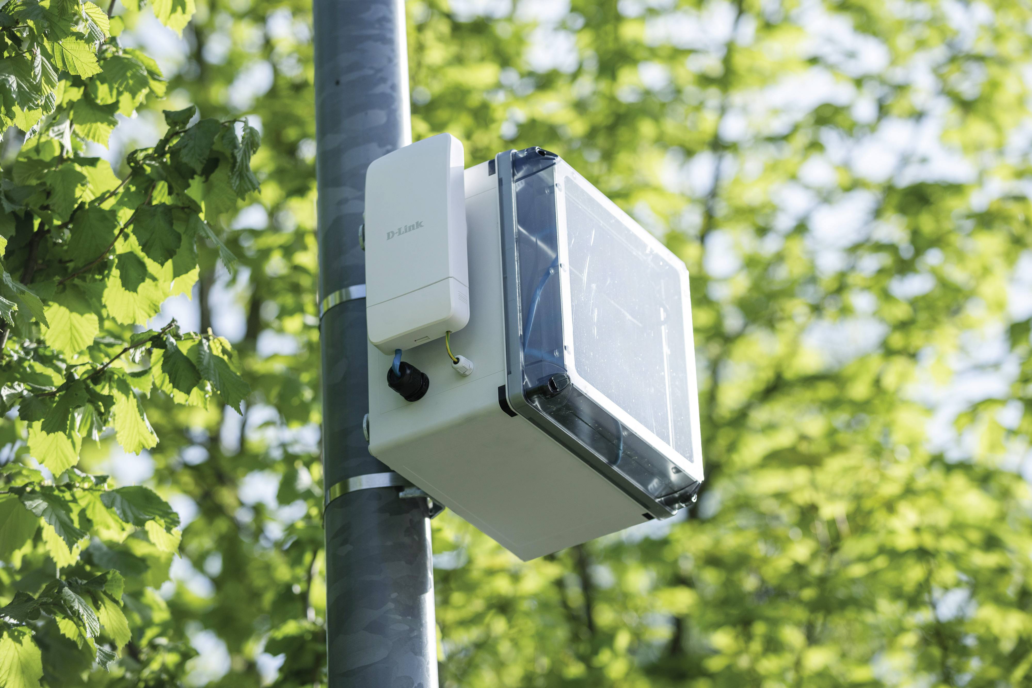 Ein Sensor an einem Mast im Freien, umgeben von grünen Blättern. Der Sensor überwacht wahrscheinlich Umweltbedingungen.