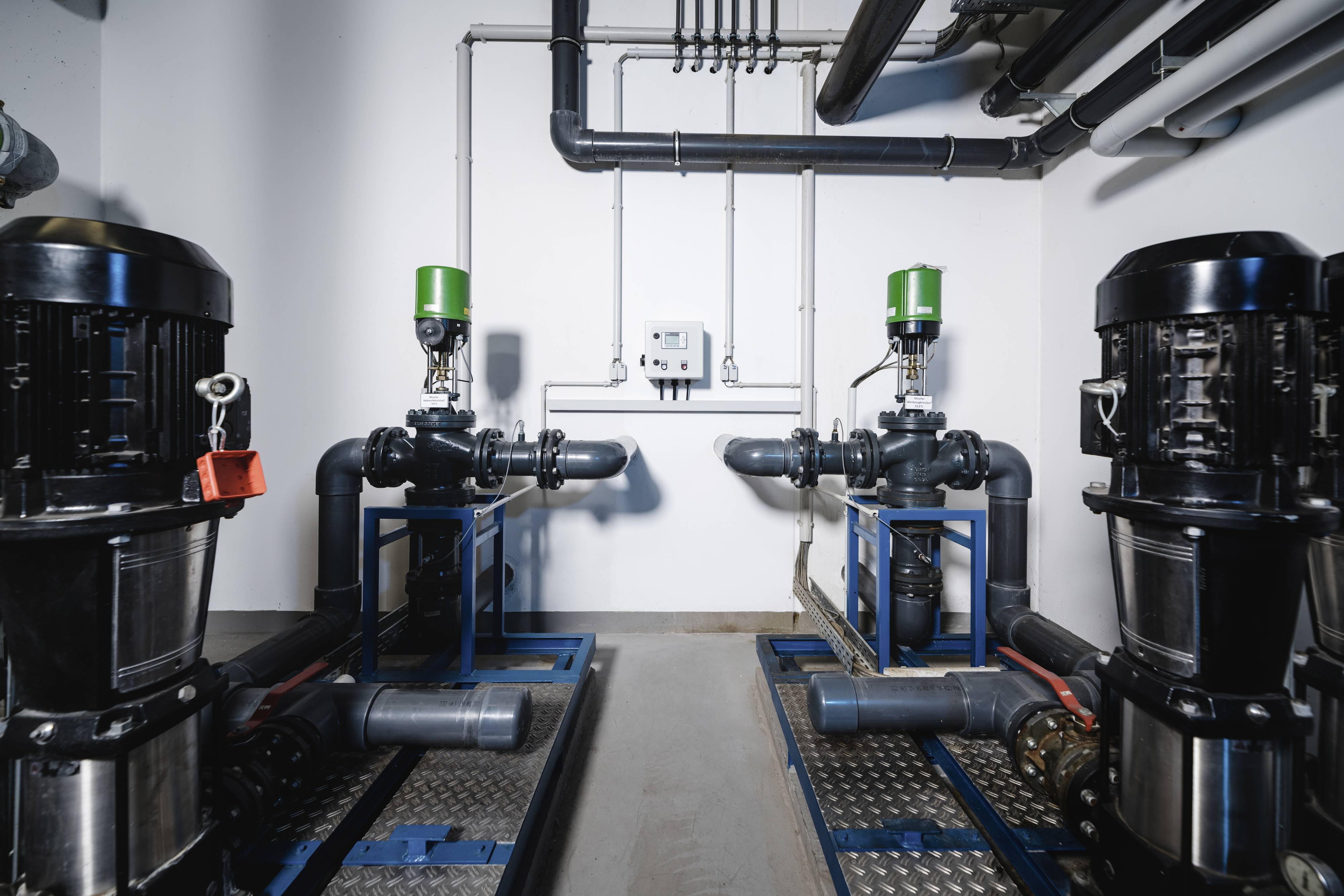 Zwei industrielle Pumpensysteme in einem technischen Raum. Sie sind symmetrisch angeordnet und mit Rohren und Ventilen verbunden.