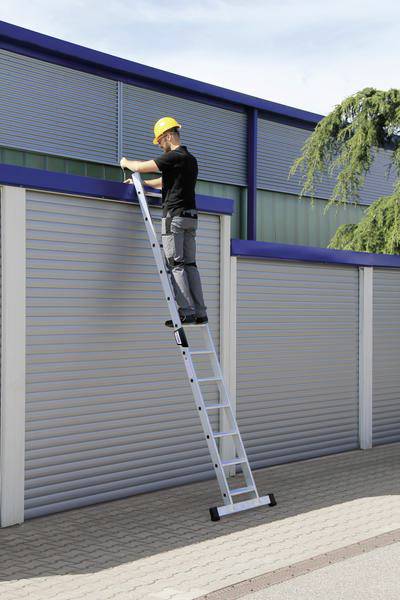 Eine Person steht auf einer Aluminiumleiter und arbeitet an Rollläden an einem Gebäude. Sie trägt einen gelben Schutzhelm.