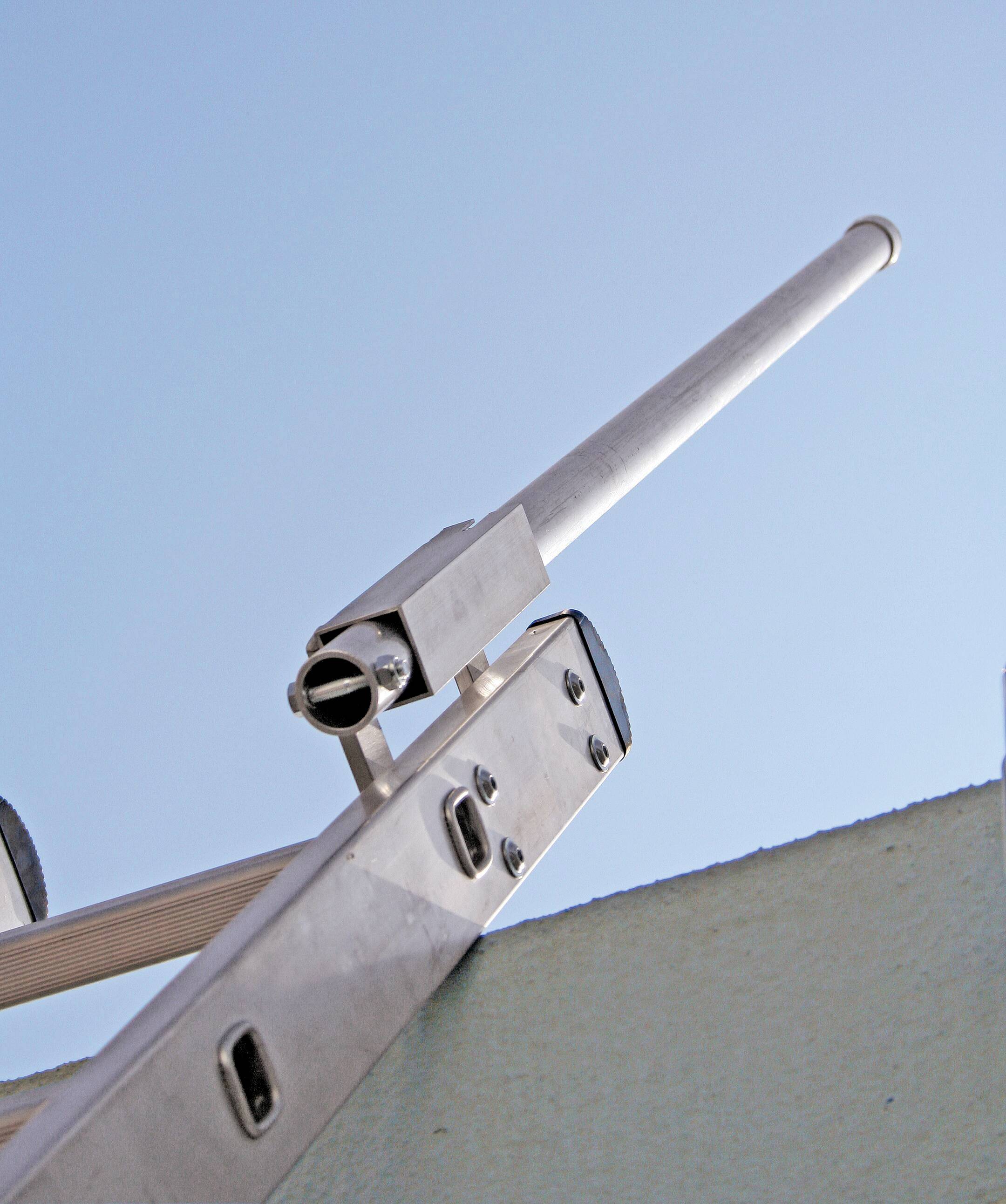 Eine lange, metallische Antenne ist an einem Mast befestigt und ragt in den blauen Himmel, möglicherweise für Signalübertragung.