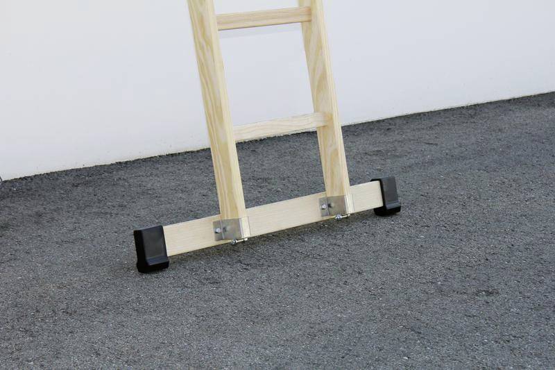 Holzleiter mit schwarzen Gummifüßen steht sicher auf einer asphaltierten Fläche.