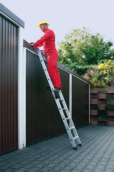 Ein Mann in roter Arbeitskleidung und gelbem Helm steht auf einer Leiter, die an einem Garagentor lehnt. Er arbeitet am oberen Rand der Garage.