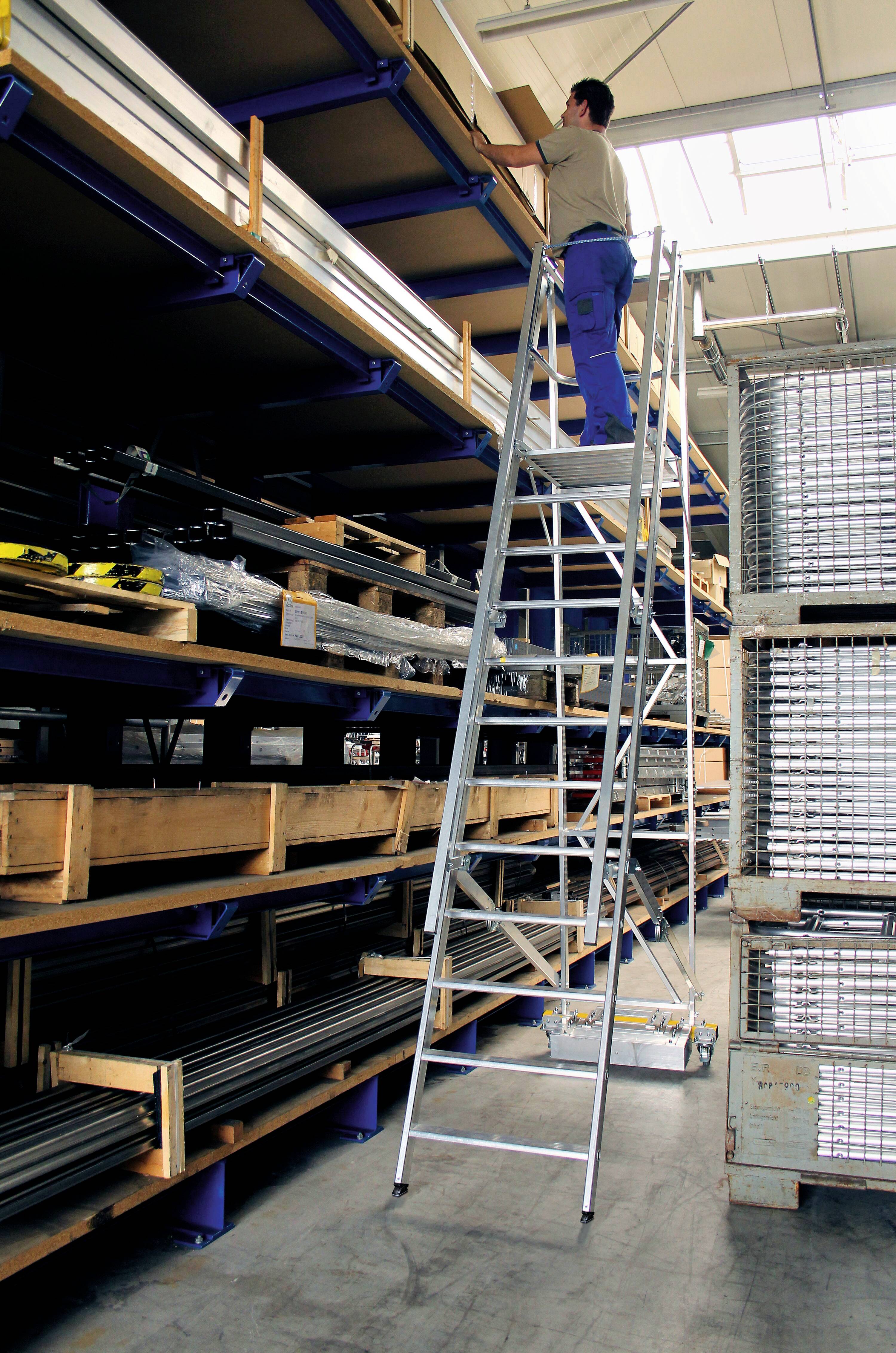 Eine Person auf einer Leiter in einem Lagerhaus erreicht ein hohes Regal. In den Regalen sind diverse Materialien und Werkzeuge gelagert.