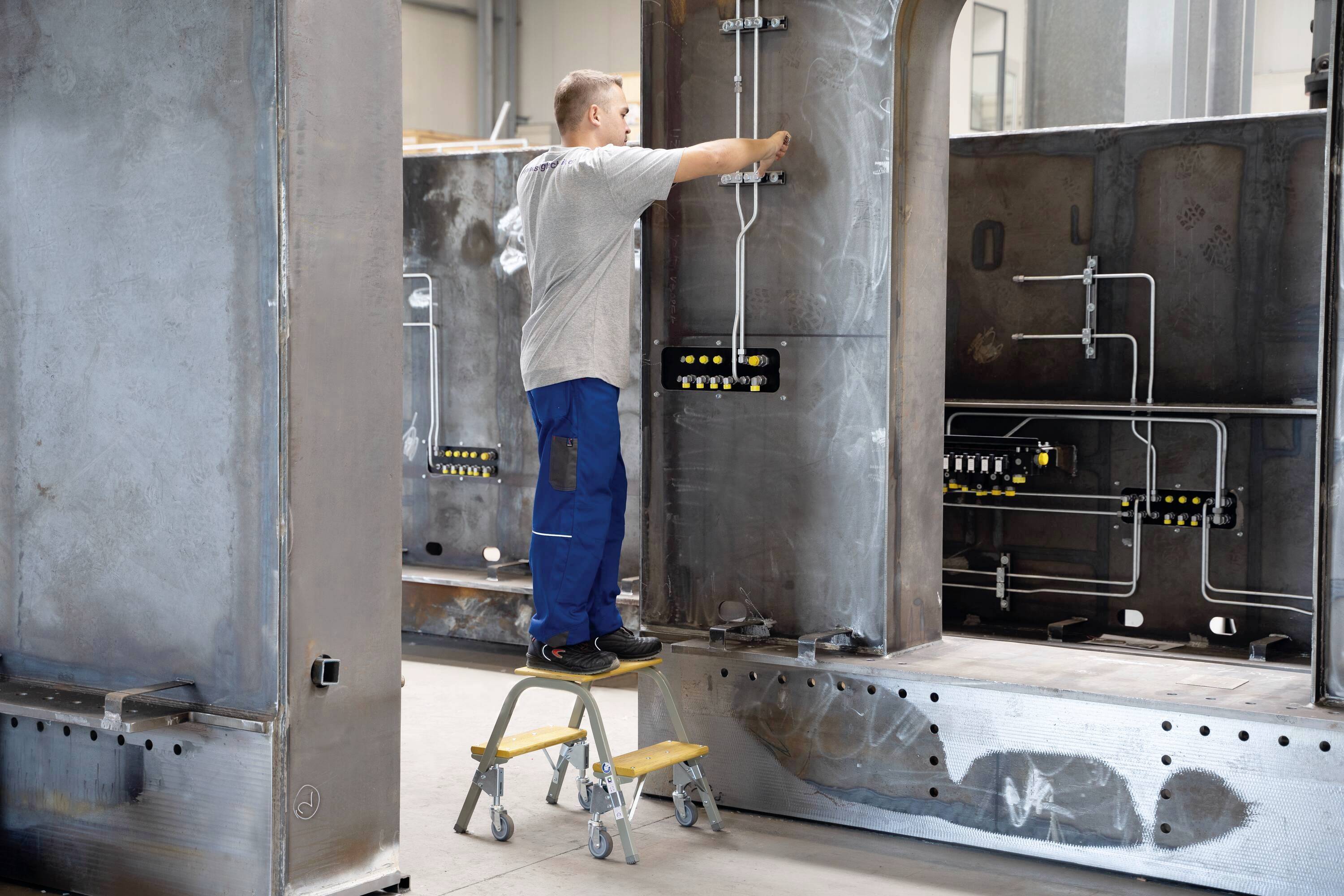 Ein Mann steht auf einem Trittbrett und arbeitet an einer großen Metallstruktur, an der Rohre und Ventile befestigt sind.