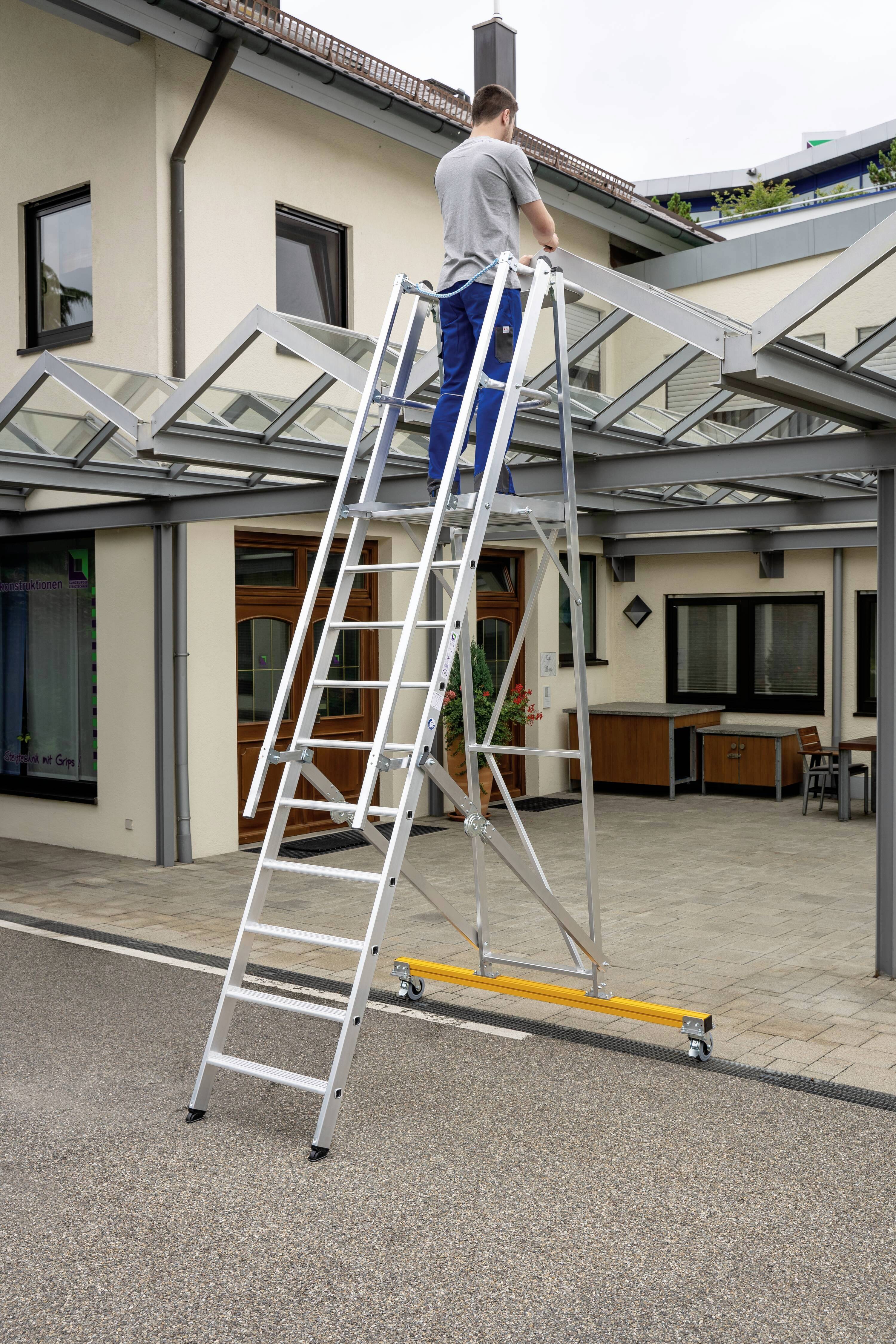 Eine Person steht auf einer Leiter vor einem Haus und arbeitet am Glasdach des Eingangsbereichs.