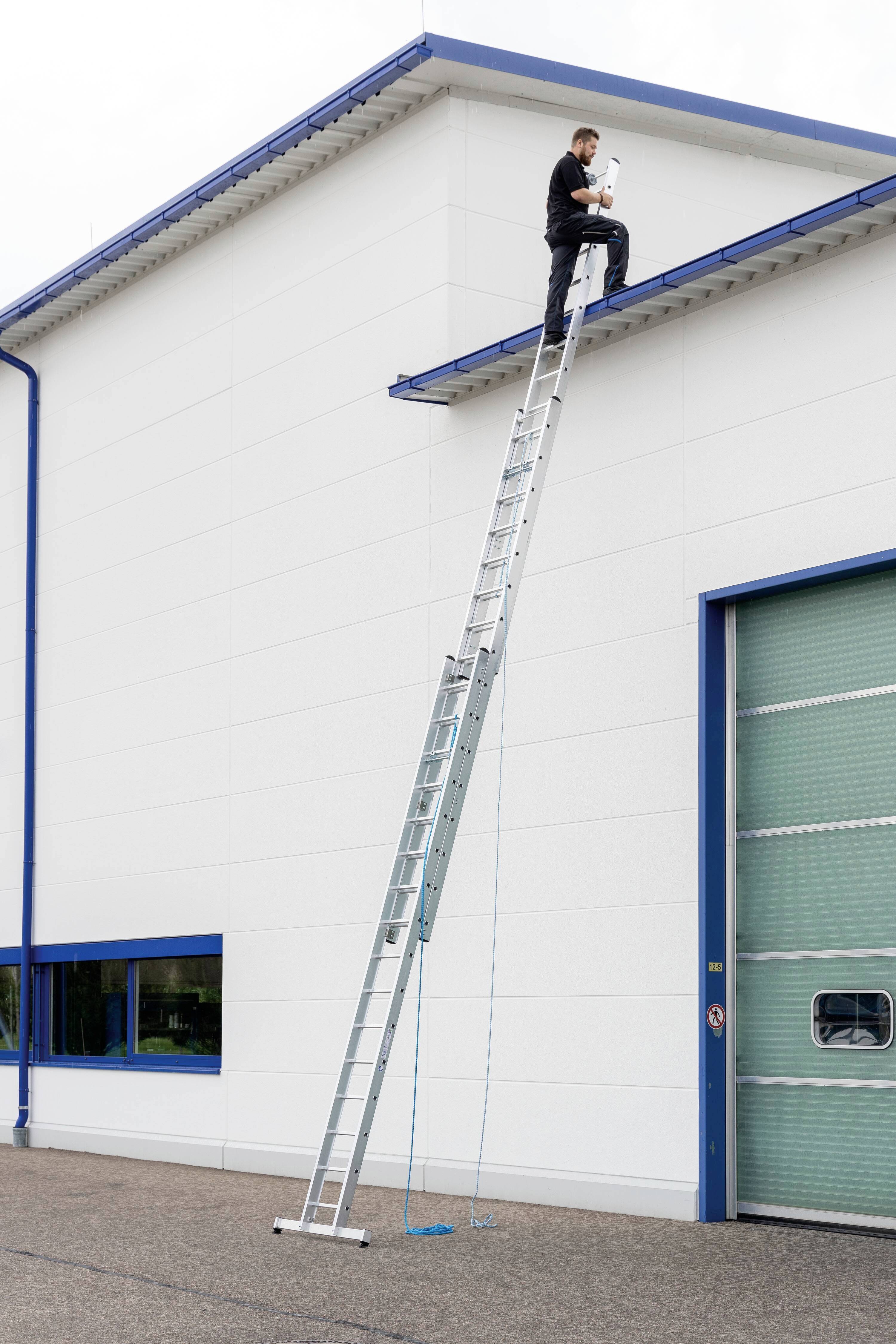 Eine Person steht auf einer hohen Leiter an der Dachkante eines Gebäudes und führt Arbeiten aus. Die Szene wirkt riskant.
