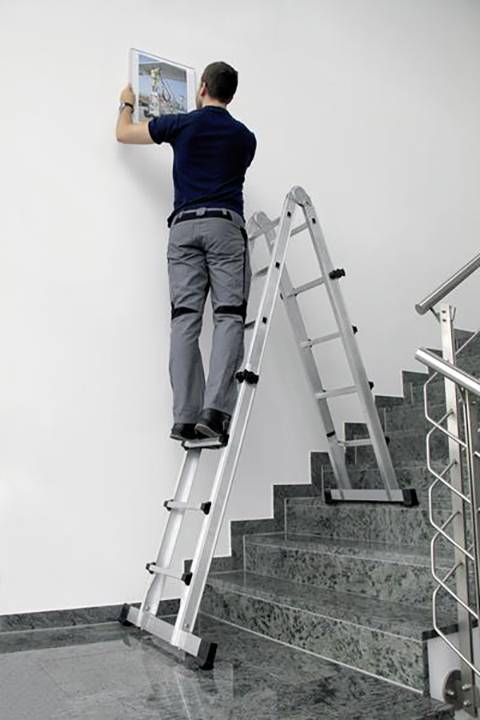 Eine Person steht auf einer Leiter auf einer Treppe und hängt ein Bild an die Wand.