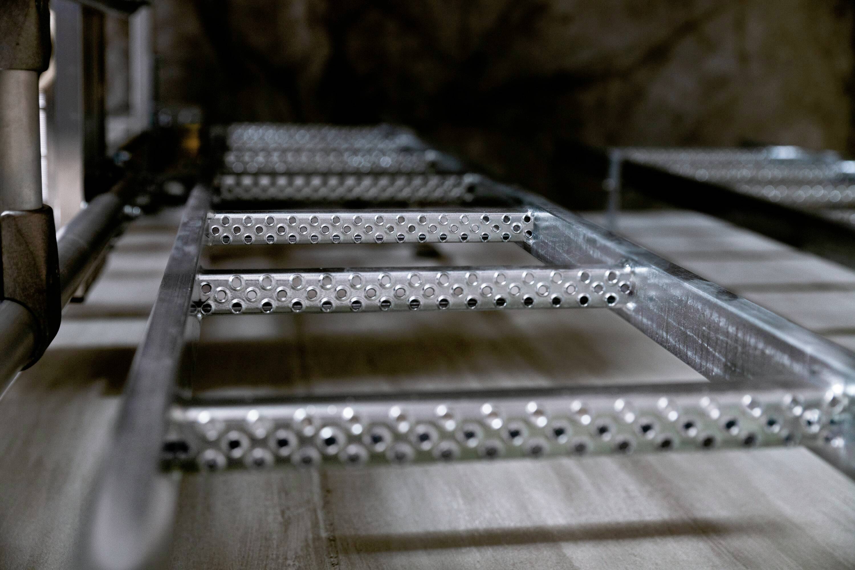 Eine Metallleiter, flach liegend mit Fokus auf die Stufen. Im Hintergrund ist ein unscharfer Stein oder Beton.