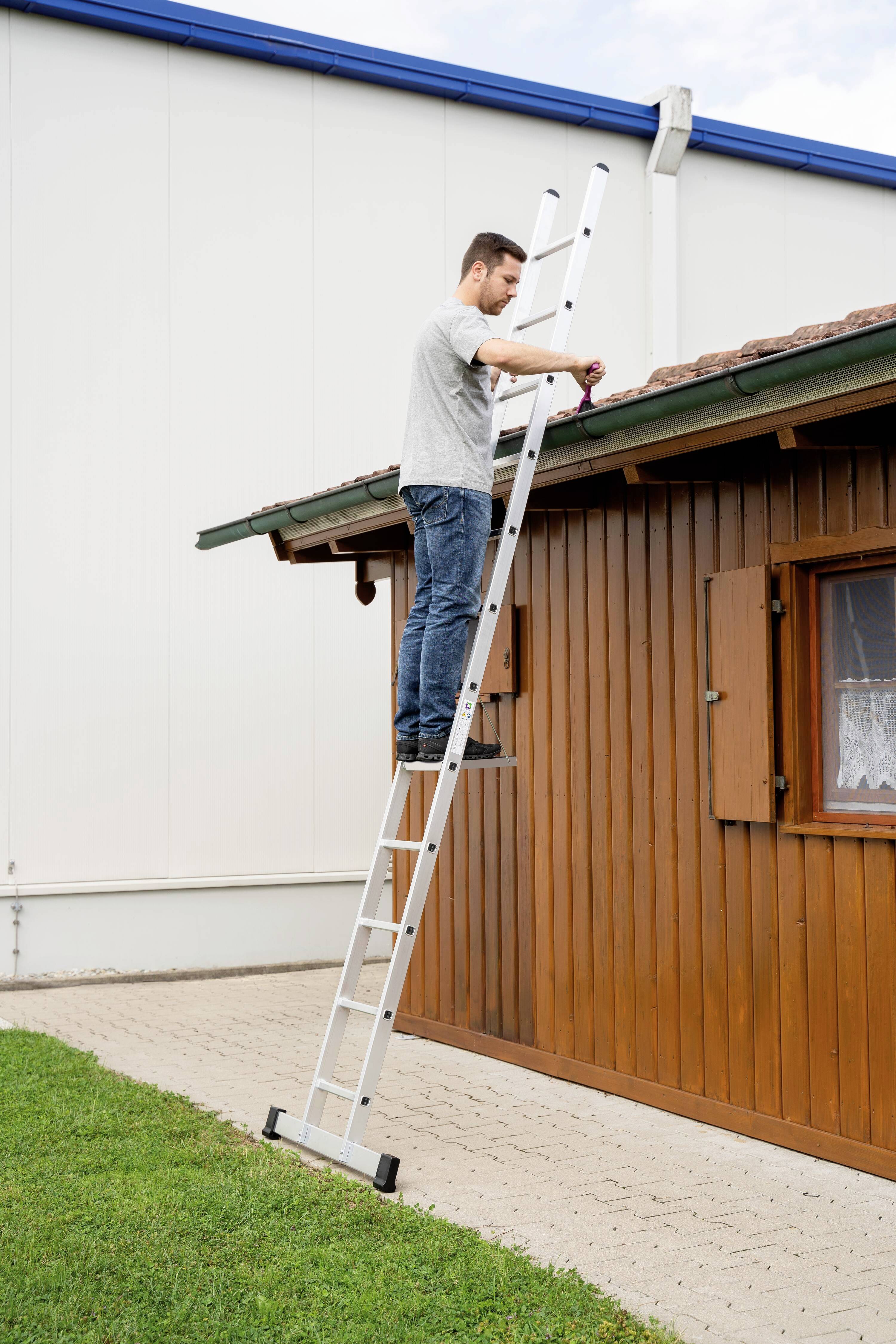 Ein Mann steht auf einer Leiter und repariert das Dach eines kleinen Holzhauses.