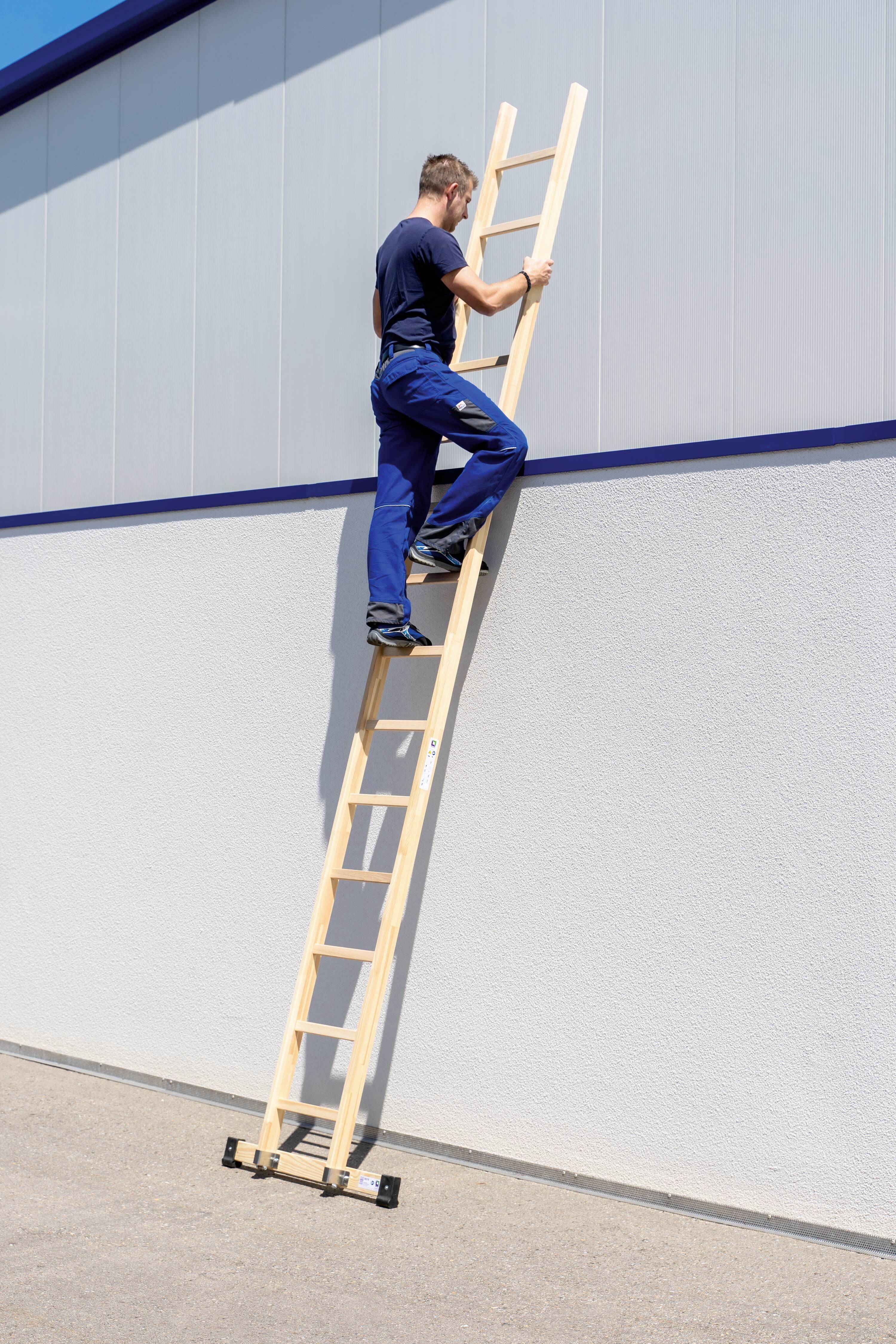 Ein Mann klettert eine Holzleiter hinauf, die an einem hohen, modernen Gebäude lehnt. Es ist ein sonniger Tag.