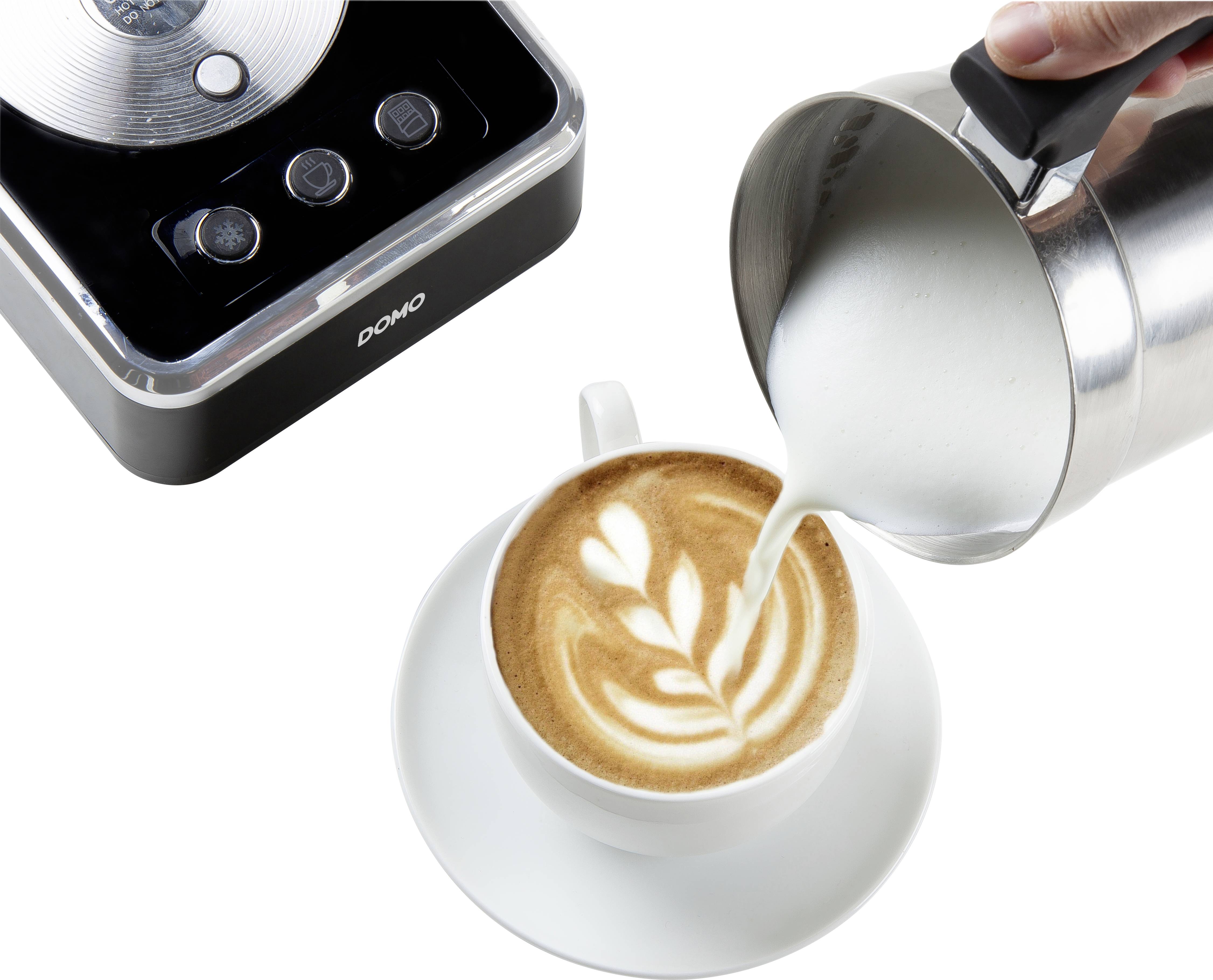 Eine Tasse Cappuccino mit Latte Art wird mit aufgeschäumter Milch aus einem Edelstahlkrug ergänzt. Links ist ein elektrischer Milchaufschäumer zu sehen.