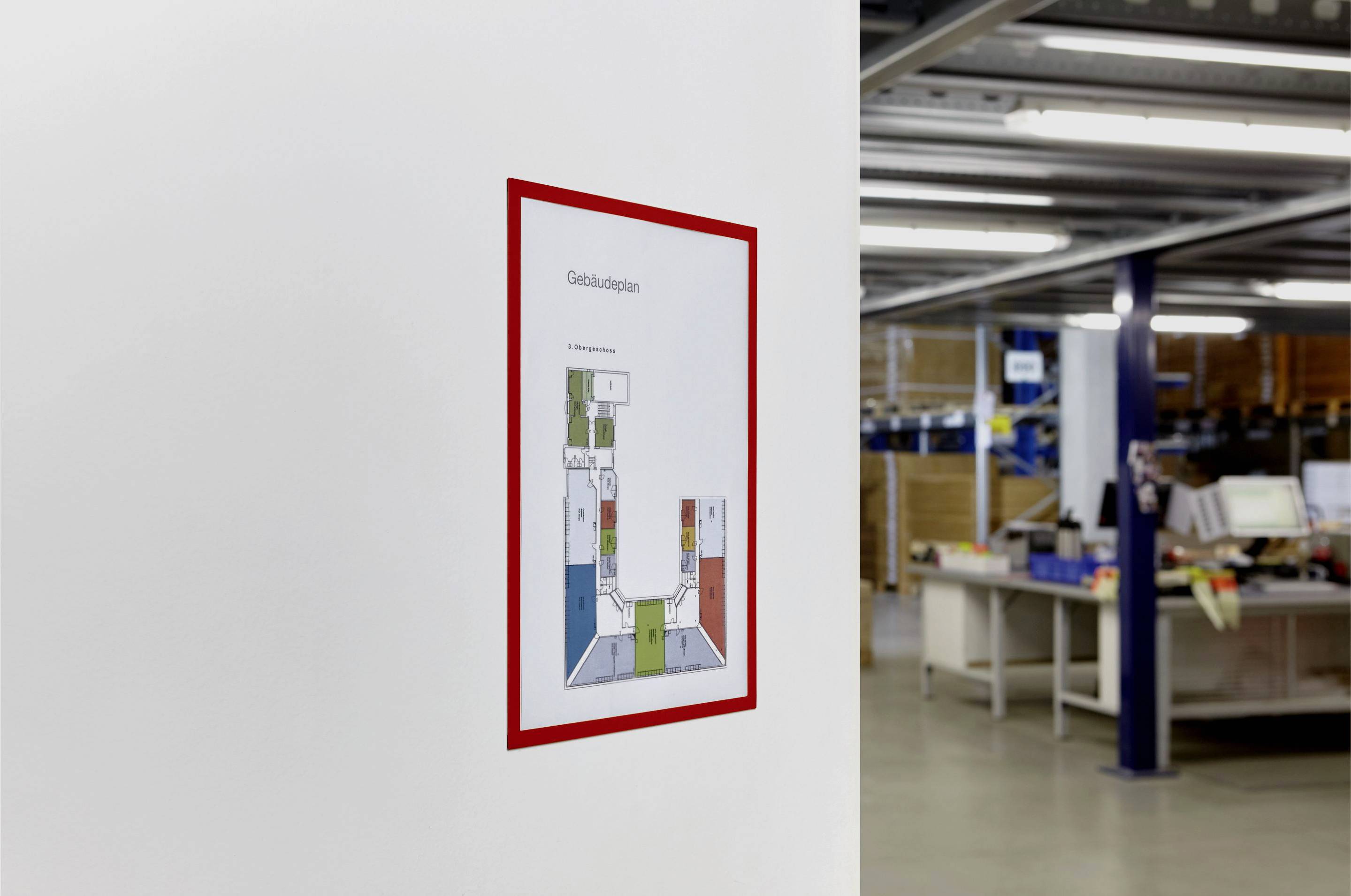 Gebäudeplan an der Wand eines modernen Büros zeigt verschiedene farbcodierte Bereiche. Büromaterialien und Tische im Hintergrund.