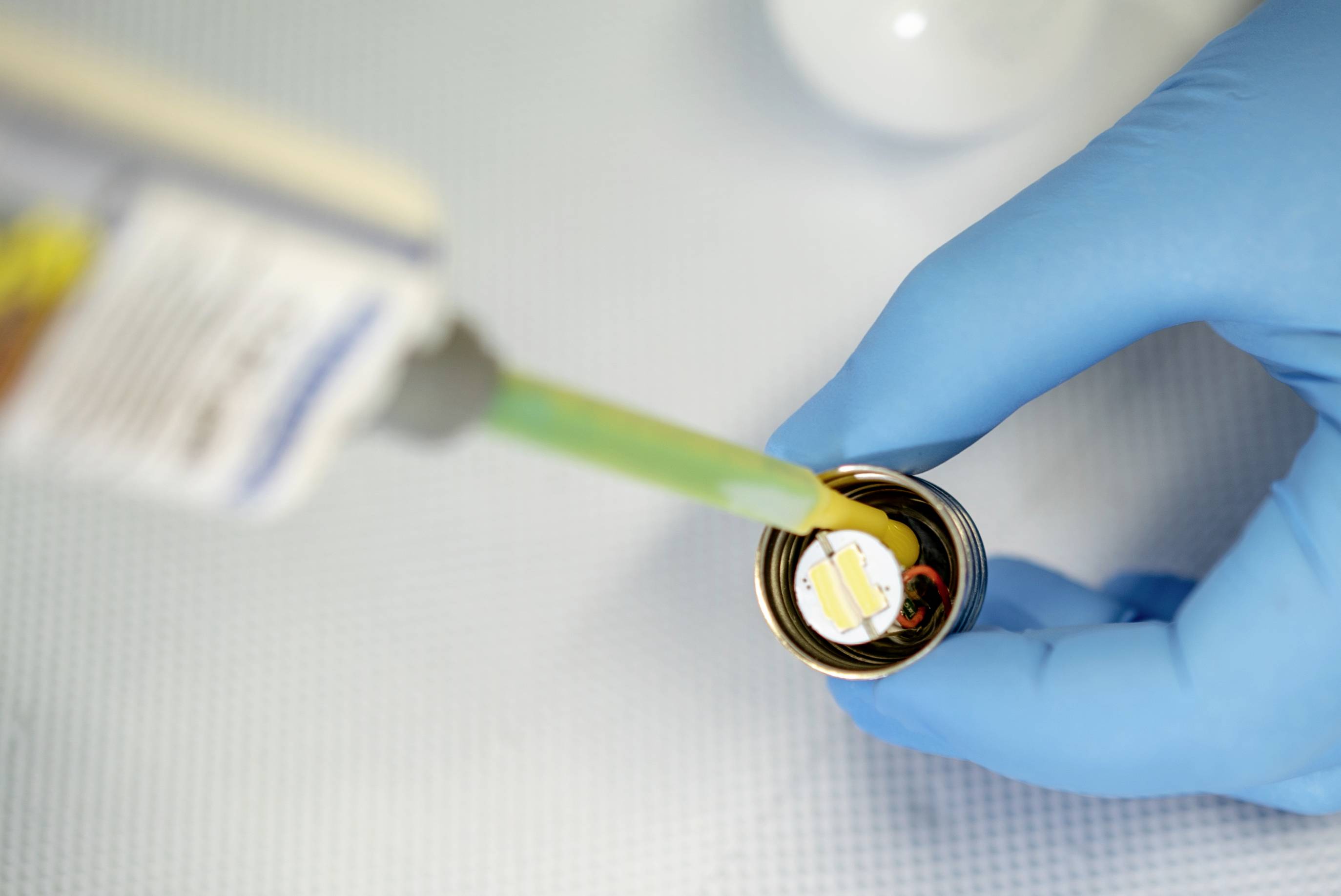 Eine behandschuhte Hand hält einen kleinen Deckel, während Klebstoff aus einer Tube darauf aufgetragen wird.