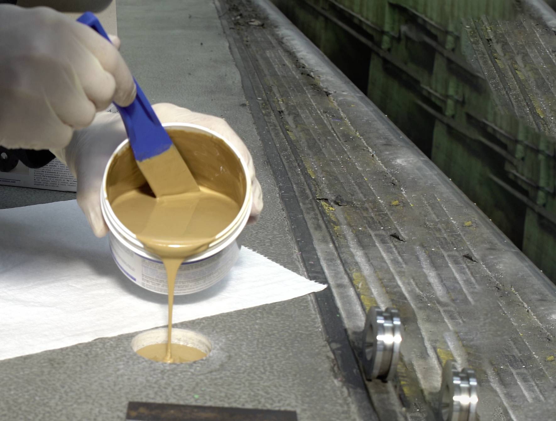 Eine Person trägt mit einem Pinsel hellbraune Flüssigkeit aus einem Behälter auf eine Oberfläche auf.