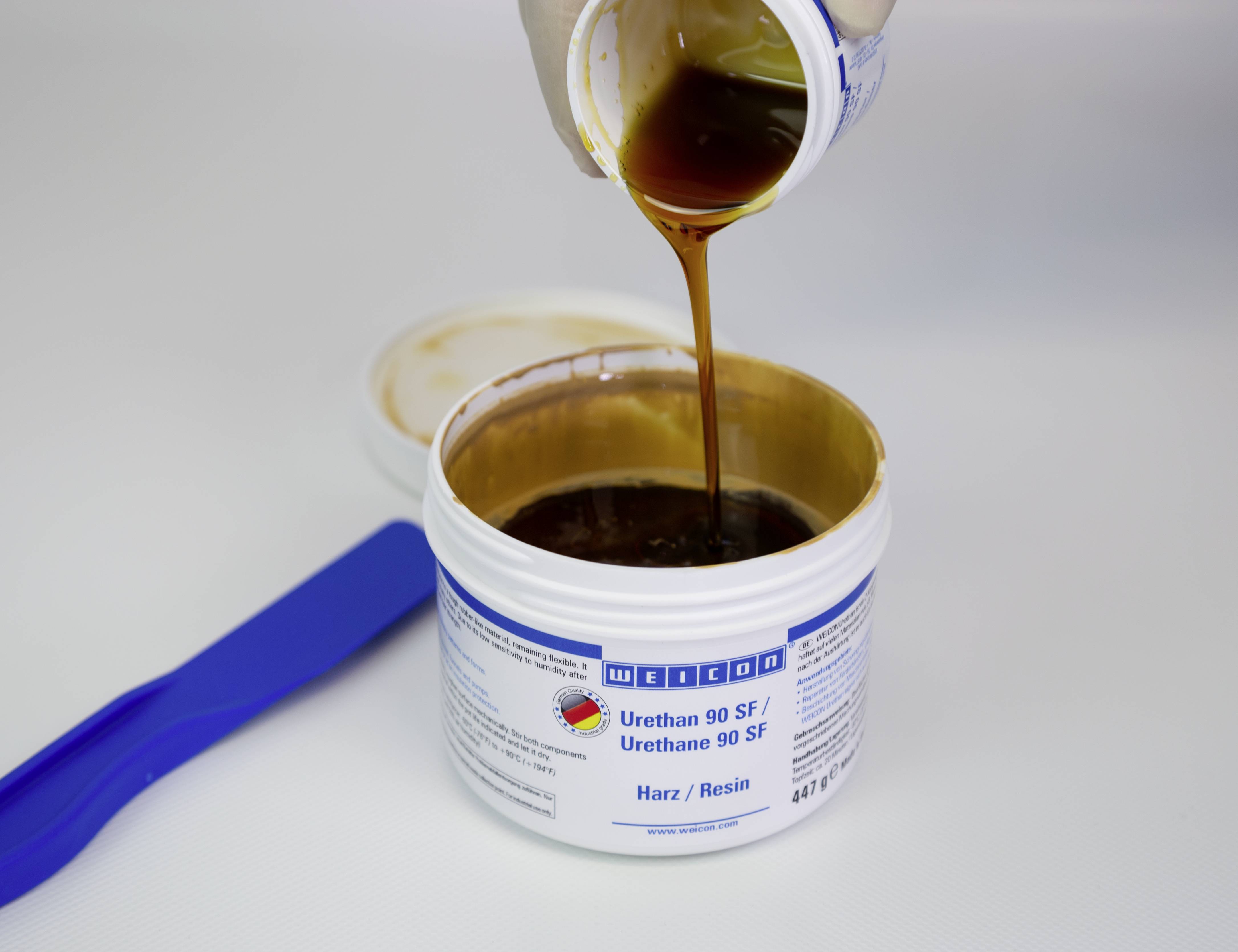 Eine dunkelbraune Flüssigkeit wird in einen offenen Behälter mit der Aufschrift 'Urethane 90 SF Harz/Resin' gegossen.