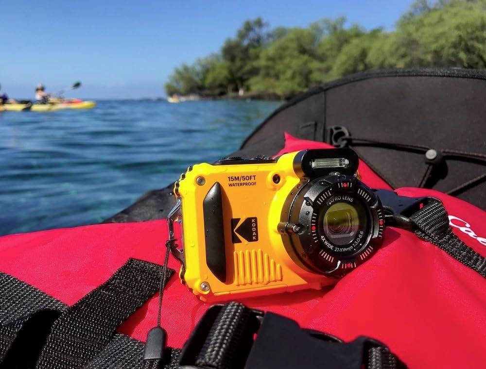 Eine gelbe wasserdichte Kamera liegt auf einer roten Schwimmweste im Kanu, mit blauem Wasser und grünen Bäumen im Hintergrund.