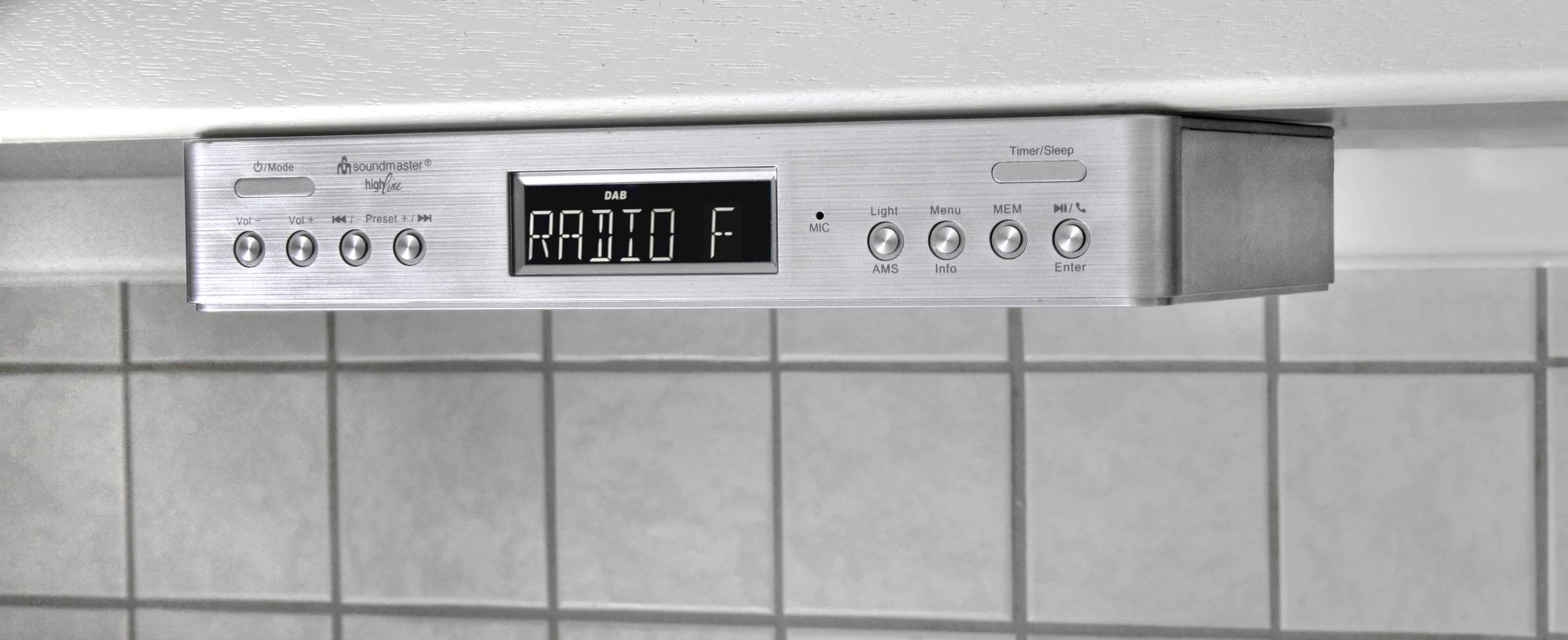 Unterbau-Küchenradio mit digitalem Display zeigt 'RADIO F'. Steuerknöpfe für Lautstärke, Senderwahl und Funktionen darunter.