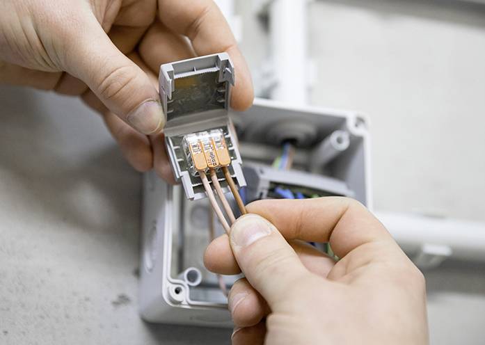 Hände verbinden Kupferdrähte in einem elektrischen Klemmenkasten.