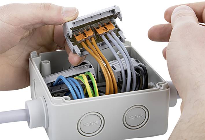 Jemand installiert Drähte in einer Verteilerdose. Die farbigen Kabel werden in Klemmen geführt, um elektrische Verbindungen herzustellen.