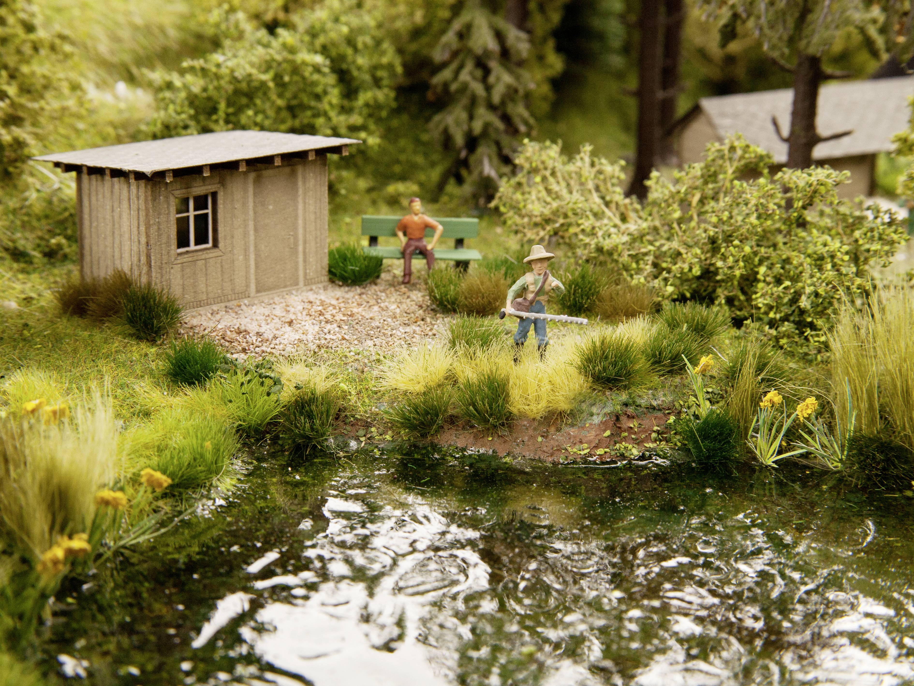 Ein Miniaturmodell zeigt eine ländliche Szene am Teich mit einem Angler im Vordergrund und einer Person auf einer Bank im Hintergrund.