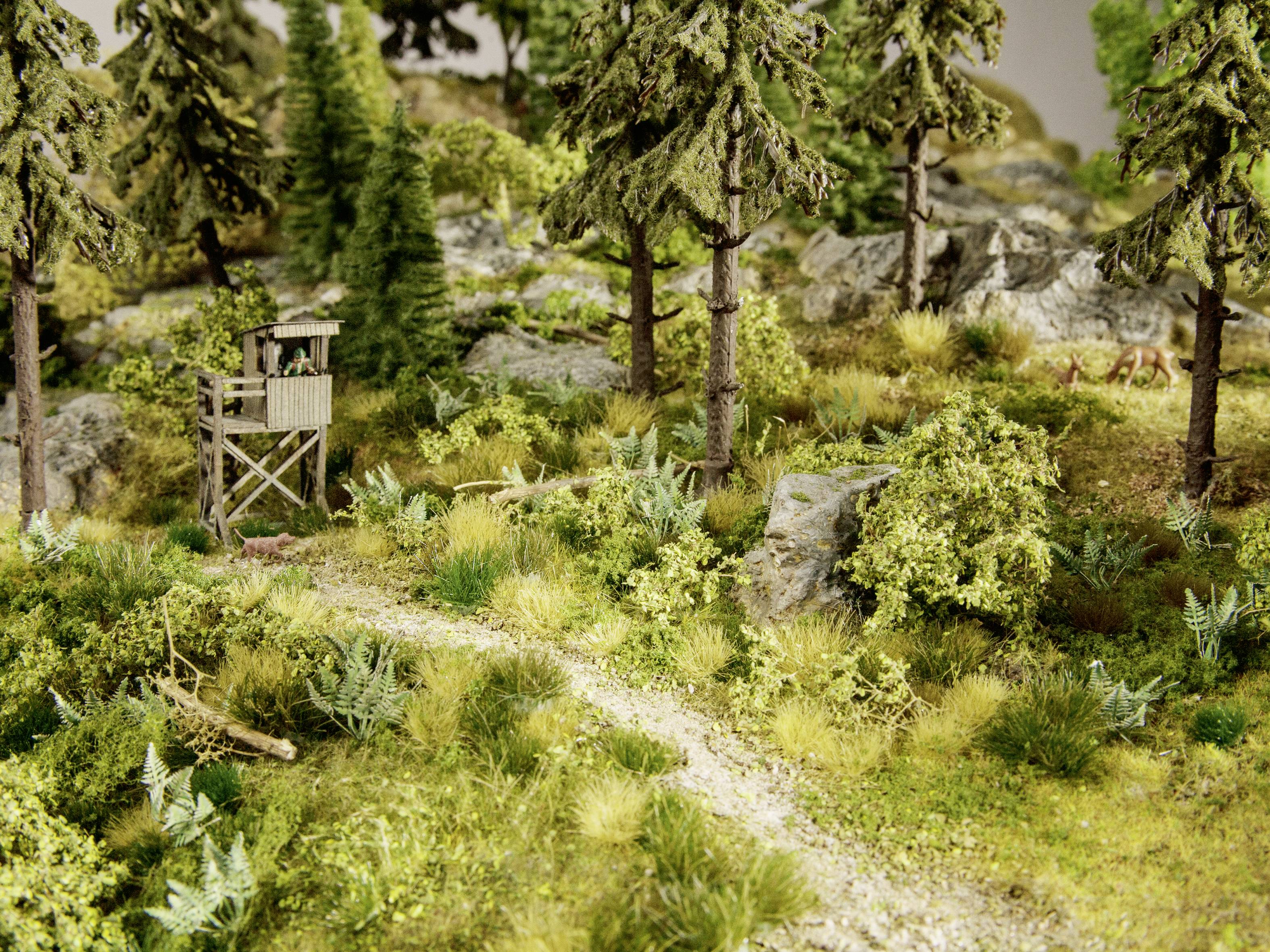 Ein Miniatur-Diorama zeigt einen Wald mit einem Hochsitz in der Nähe eines kleinen Weges, umgeben von Bäumen und Sträuchern.