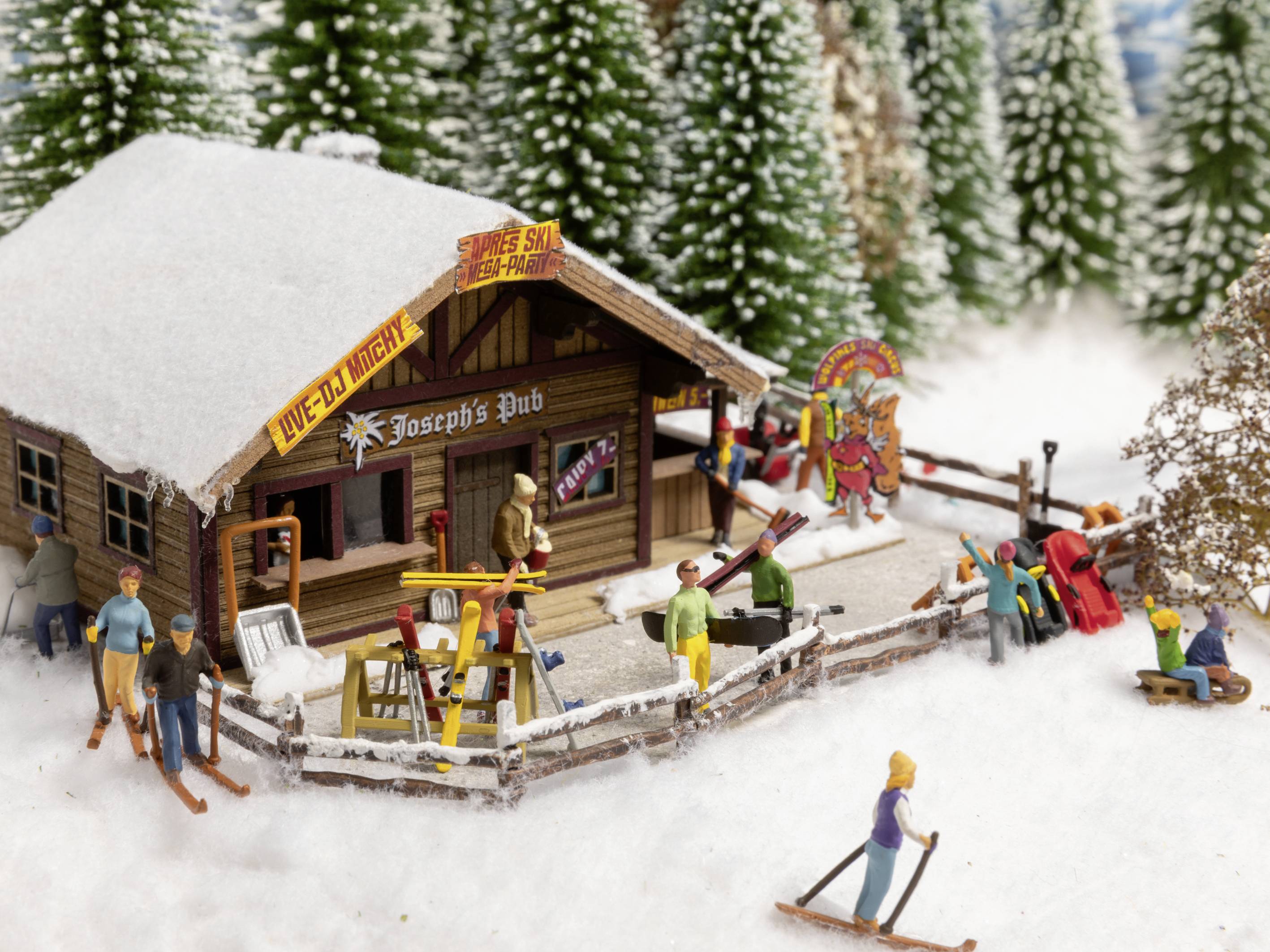Eine verschneite Miniaturszene zeigt Joseph's Pub mit Skifahrern und Schneemännern. Menschen sind in Winterkleidung beschäftigt.