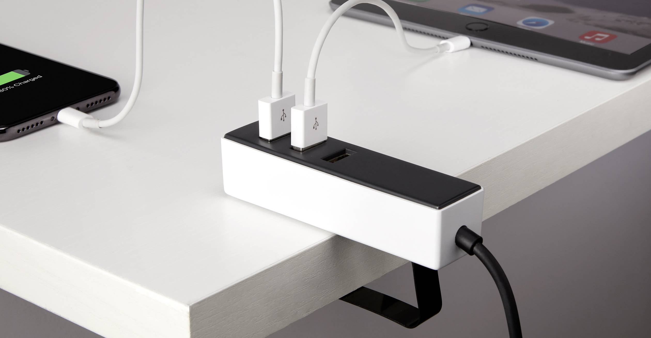 Ein Kabelklemmen-Organizer ist an einem Tisch befestigt, mit mehreren Kabeln verbunden, die verschiedene Geräte wie ein Tablet aufladen.