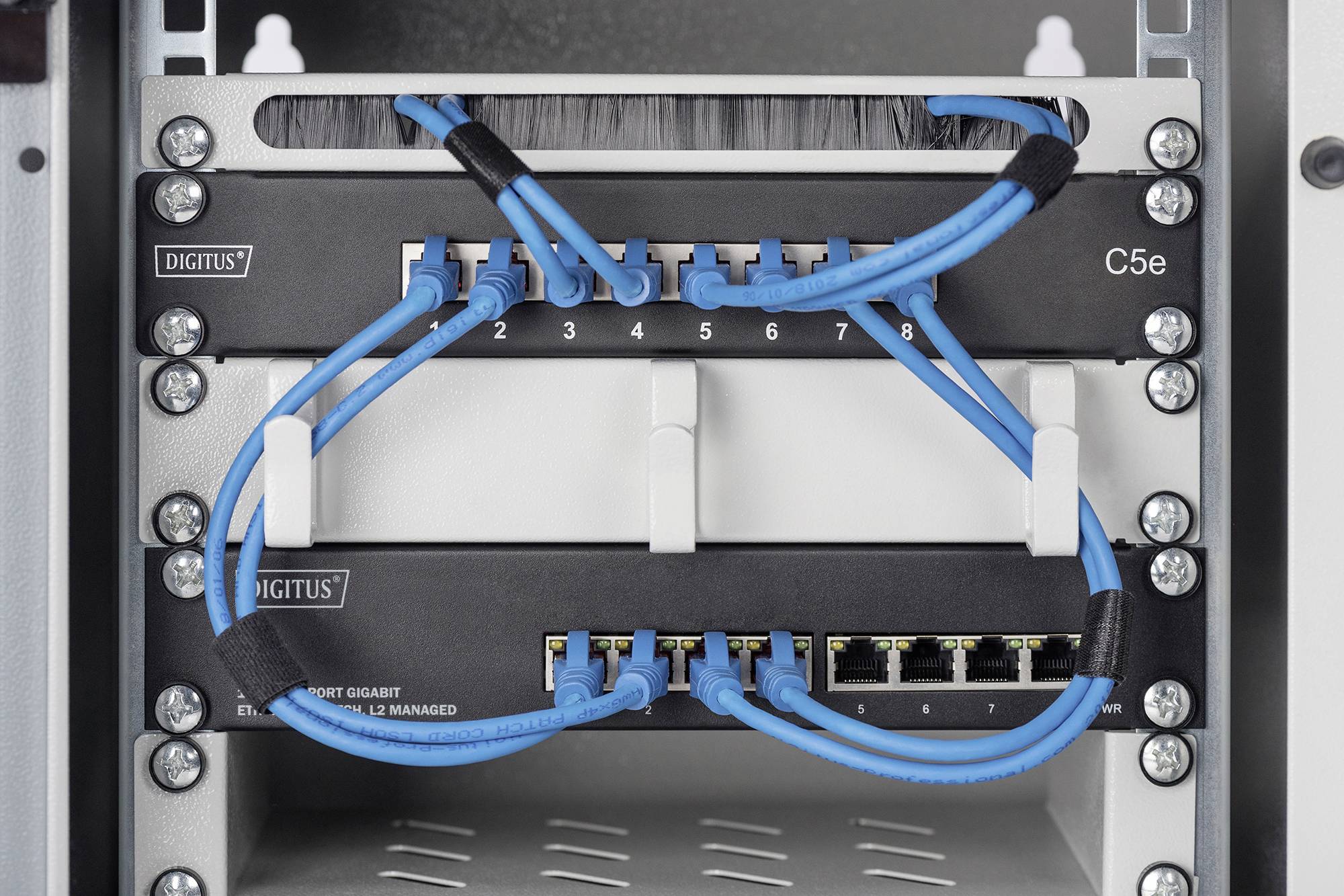 Ein Netzwerkverteilerkasten mit blauen Ethernet-Kabeln, die in einen Patchpanel und einen Switch angeschlossen sind.