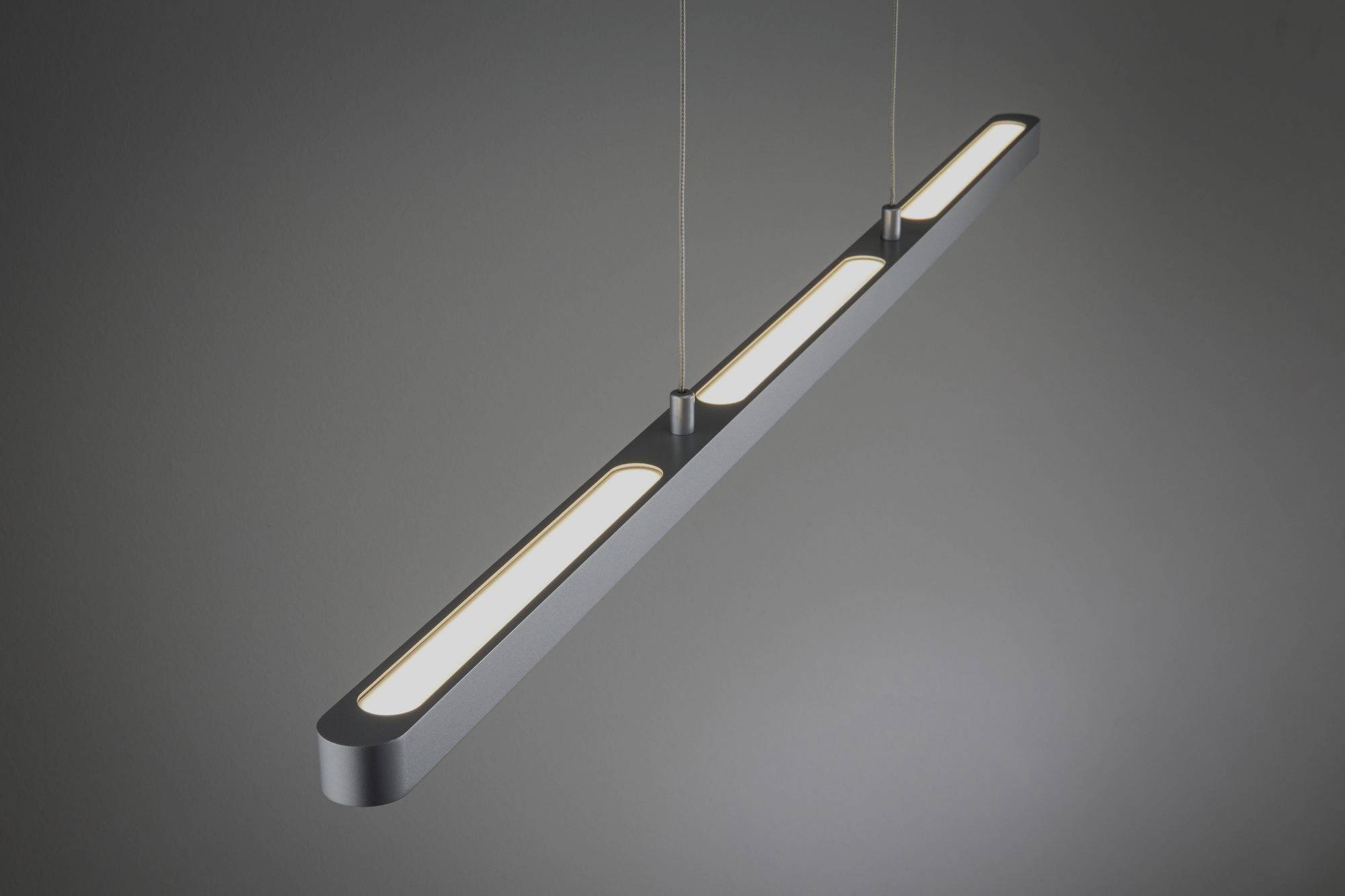 Eine moderne, hängende LED-Leuchte mit langgestrecktem, schlankem Design und drei leuchtenden Elementen in einem dunklen Raum.