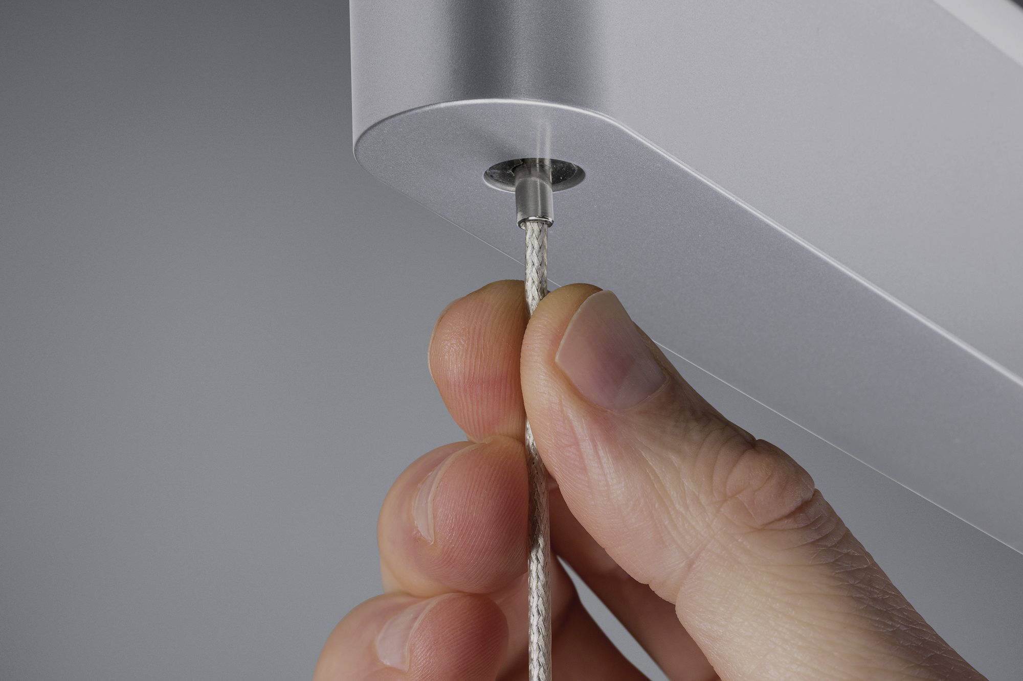 Nahaufnahme einer Hand, die ein dünnes Kabel in ein silbernes Gerät einführt.