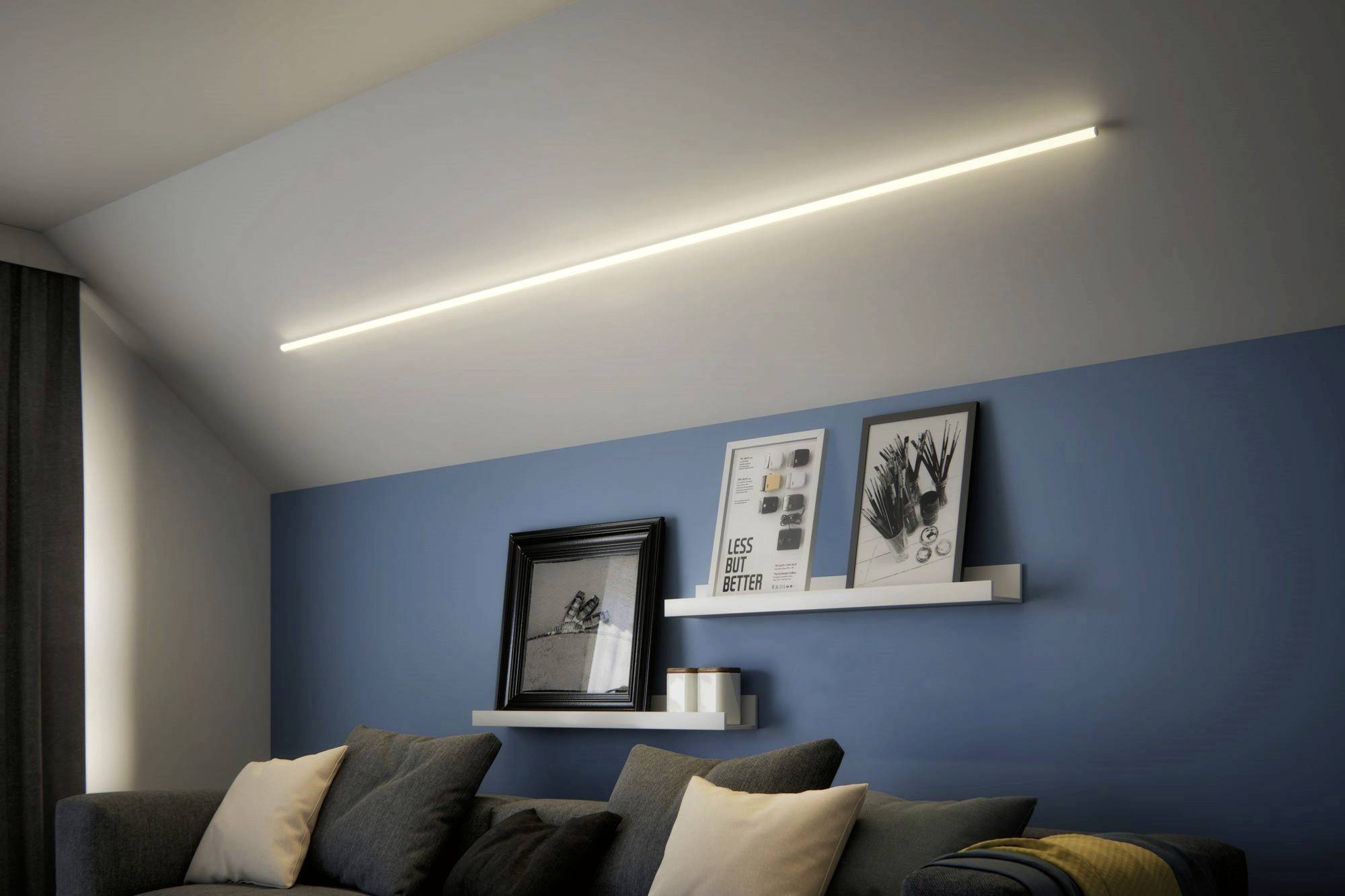 Wohnzimmer mit blauer Wand, beleuchtet durch eine lange, horizontale Leuchte an der Decke. Zwei Regale mit Bildern und Kerzen über einem grauen Sofa.