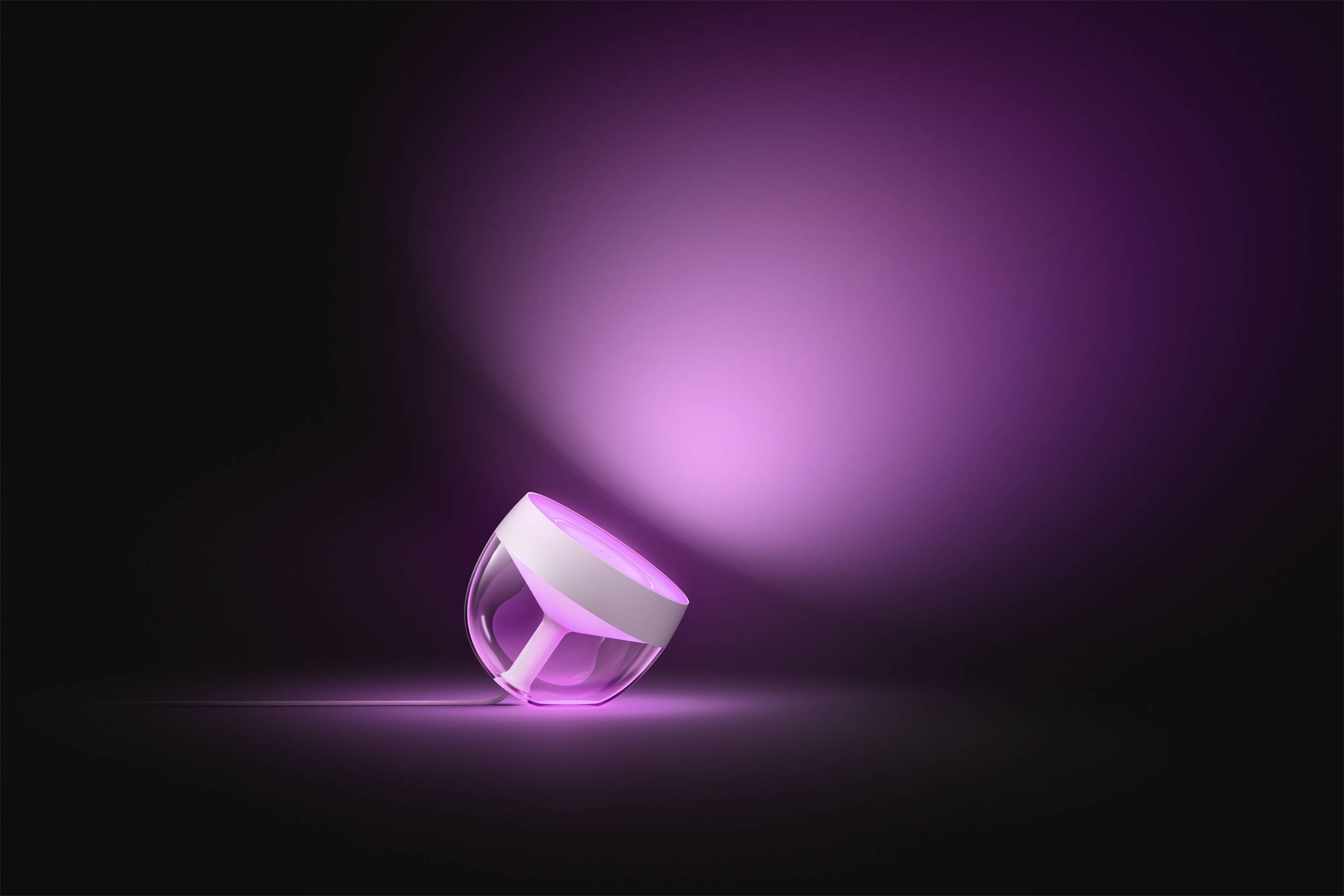 Eine kleine, runde Lampe mit transparentem Gehäuse leuchtet in intensivem Rosa und projiziert Licht auf einen schwarzen Hintergrund.