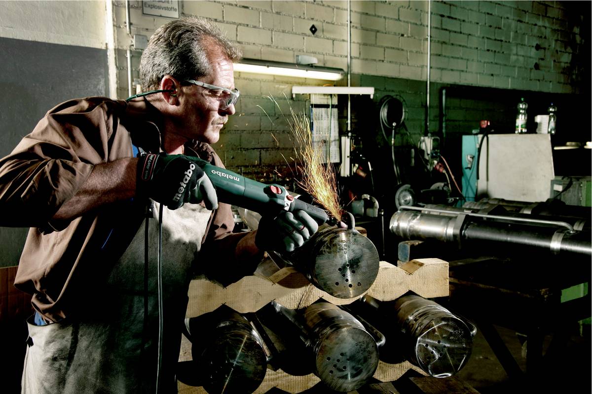 Ein Mann in einer Werkstatt verwendet einen Winkelschleifer, um Metallrohre zu bearbeiten. Funken fliegen vom Schleifpunkt.