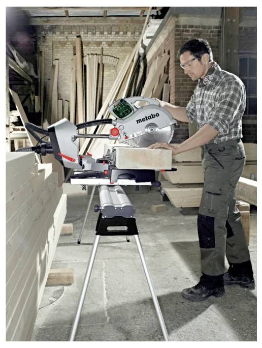 Ein Mann benutzt eine Metabo-Gehrungssäge, um ein Holzbrett in einer mit Holz gefüllten Werkstatt zu schneiden.