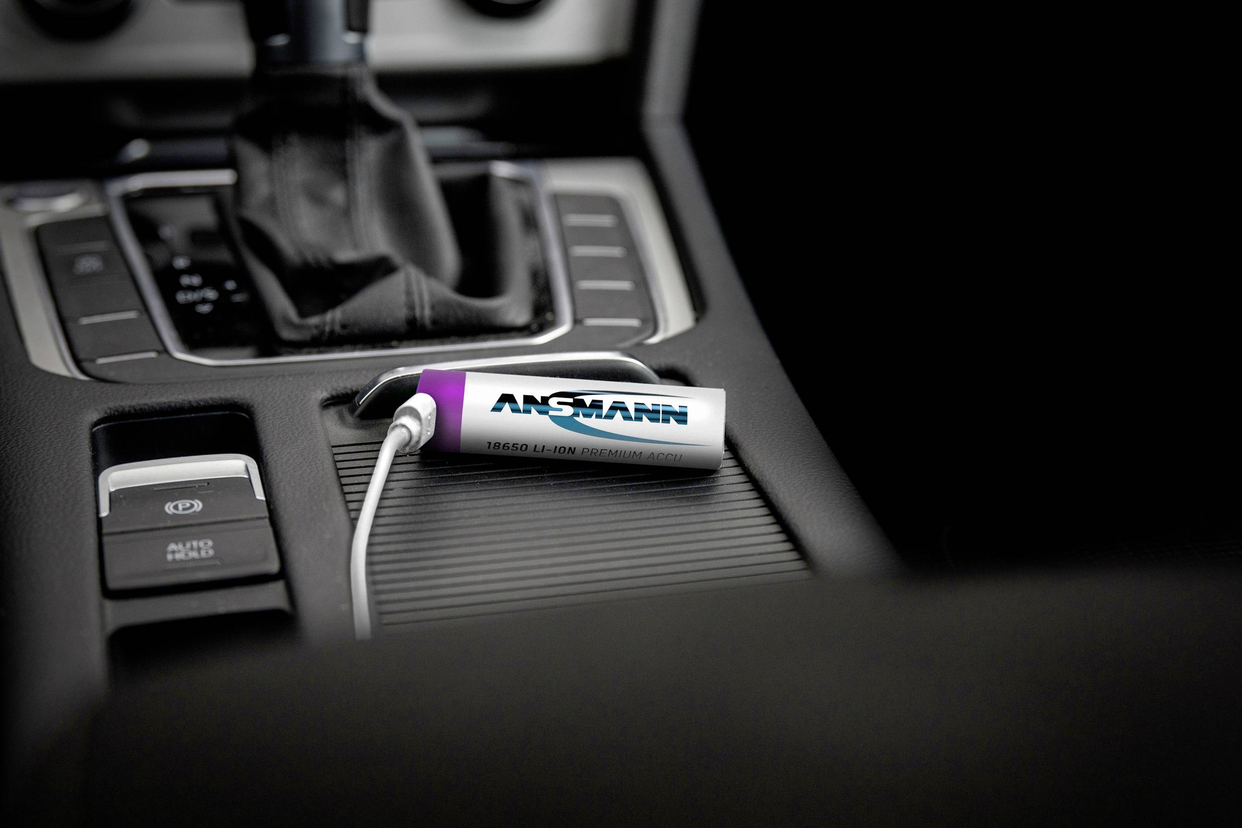 Ein silberner, tragbarer USB-Akku liegt in der Mittelkonsole eines Autos, verbunden mit einem weißen Kabel.