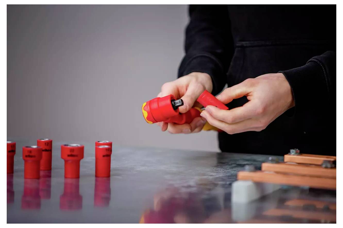 Eine Person hält einen roten elektrischen Stecker und bereitet ihn für die Verwendung vor. Mehrere Werkzeuge und Stecker sind auf der Metalltischoberfläche ausgebreitet.