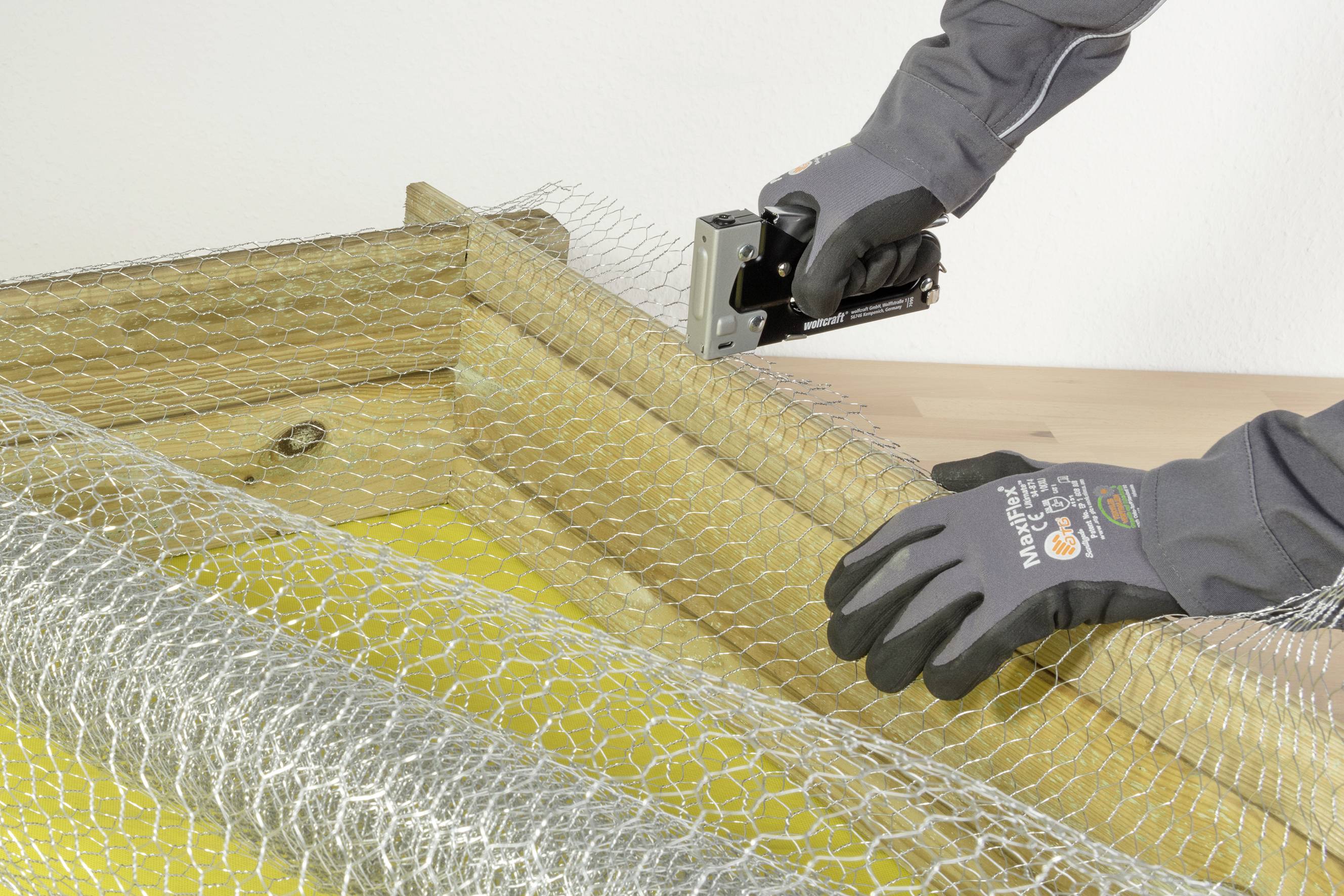 Eine Person befestigt Maschendraht mit einem Tacker an einem Holzrahmen.