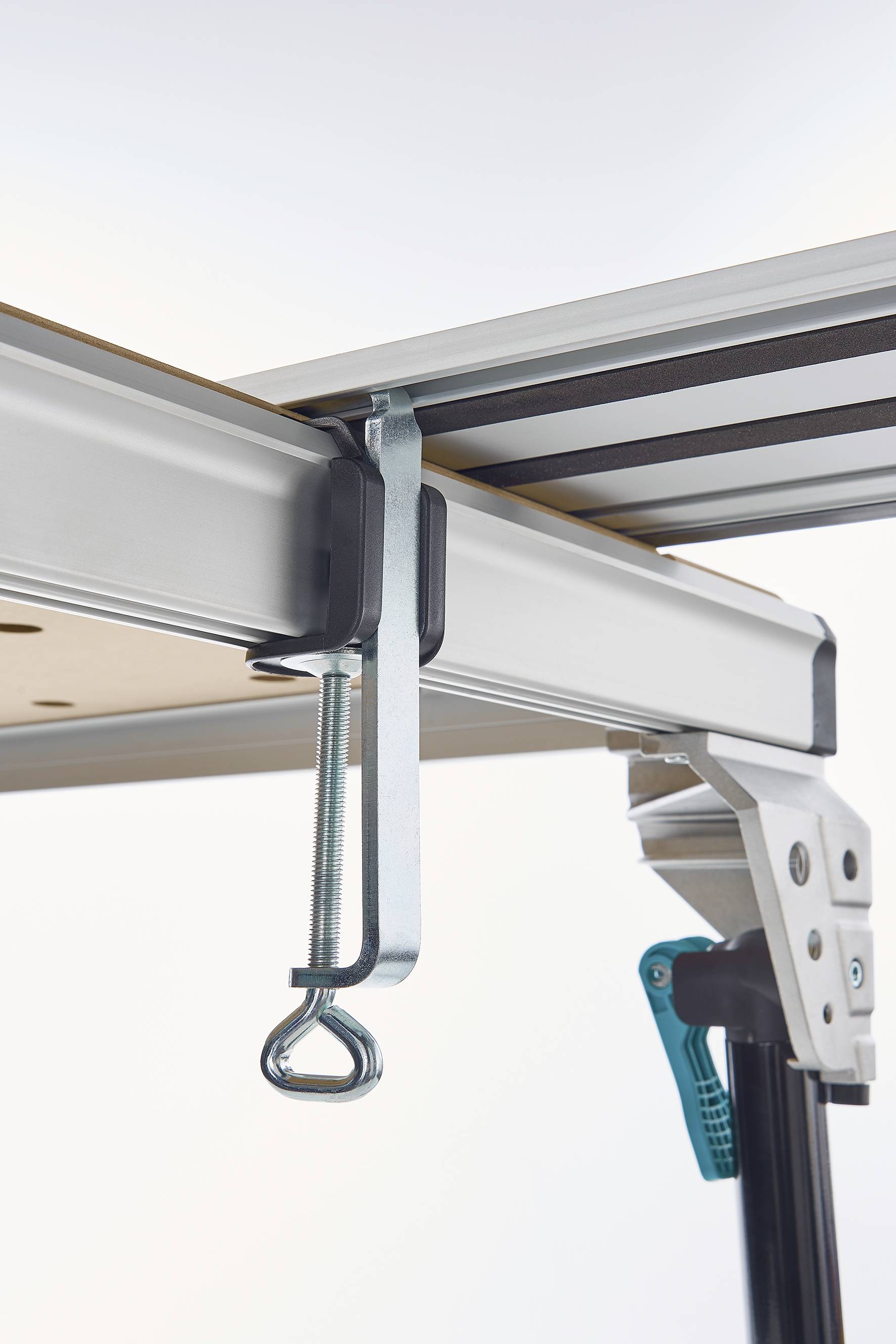 Metallklemme befestigt eine Tischplatte an einem Aluminiumrahmen. Die Klemme ist festgezogen und stabilisiert die Konstruktion.