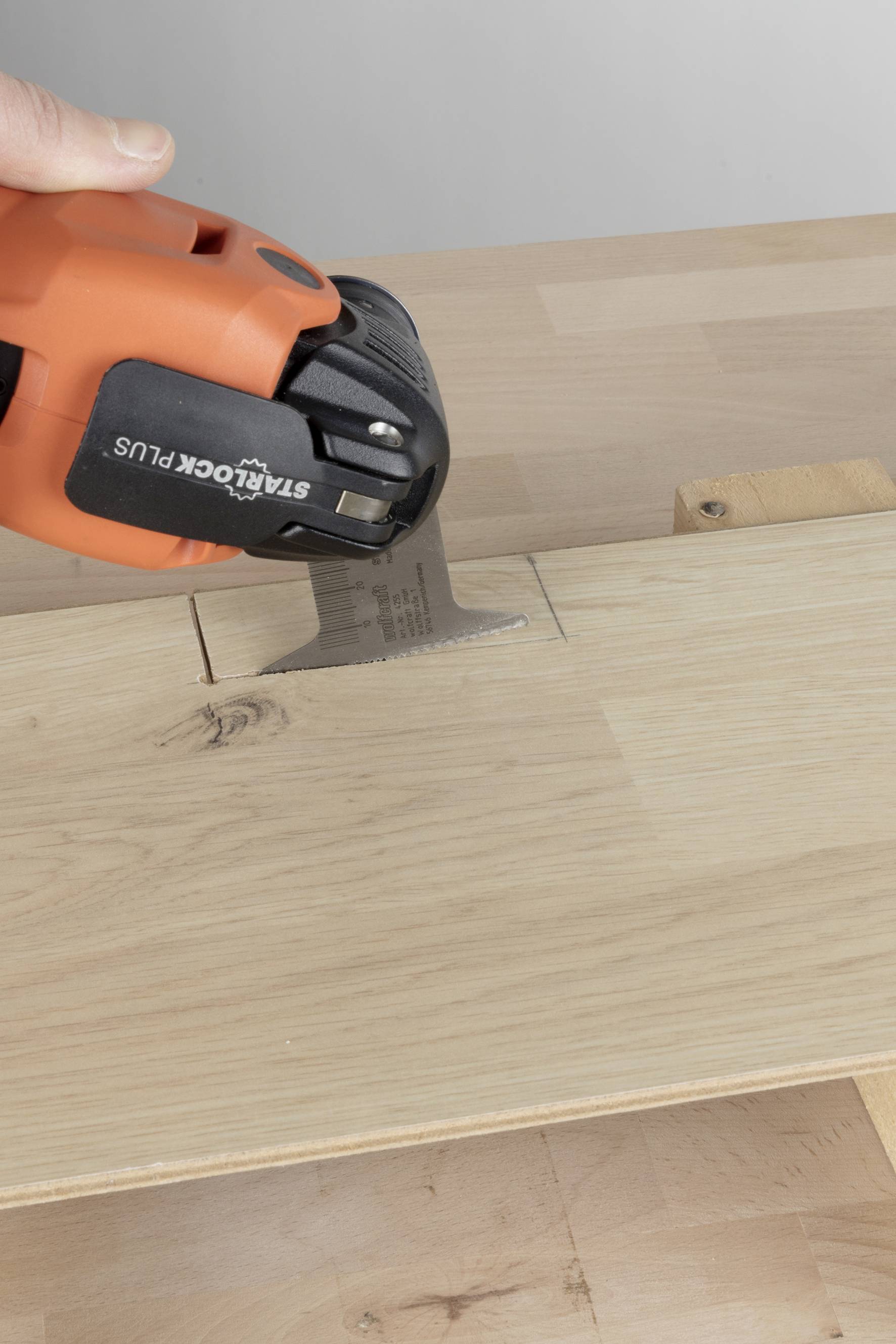 Eine Hand hält ein orangefarbenes Werkzeug, das in ein Holzbrett schneidet, um präzise Ausbesserungen oder Anpassungen durchzuführen.