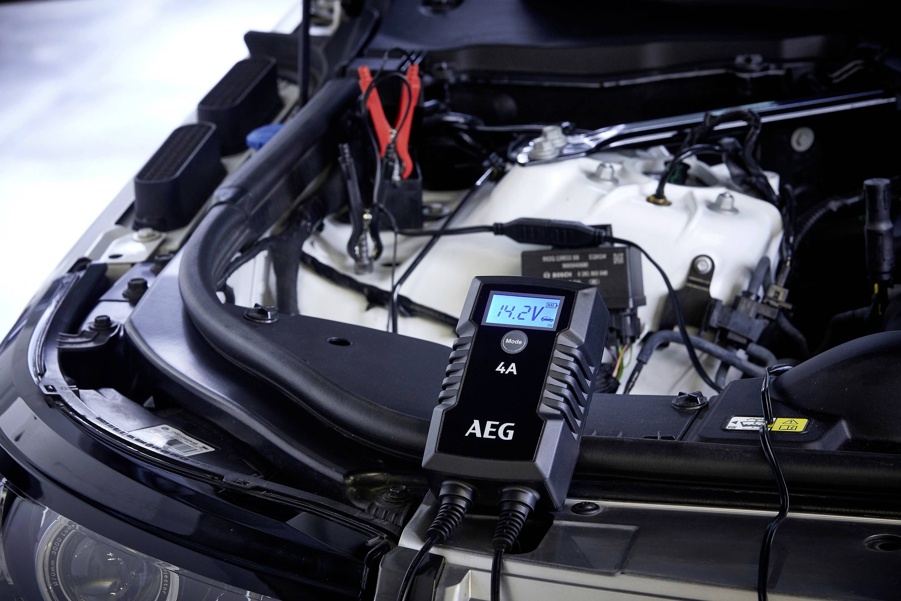 Ein Autoladegerät von AEG ist an die Autobatterie angeschlossen, zeigt eine Spannung von 14,2 V an und wird getestet.