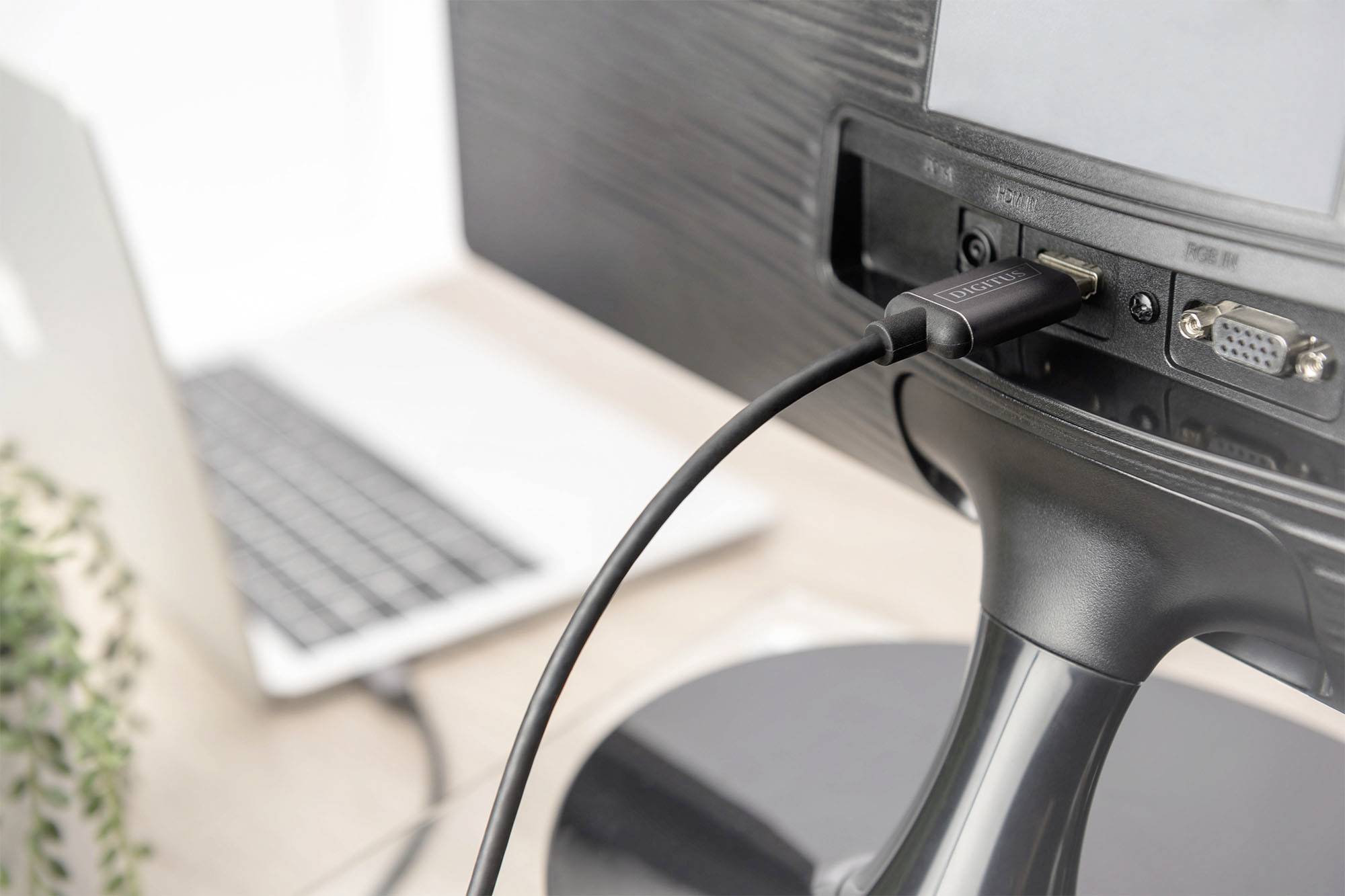 Ein Computerbildschirm ist über ein HDMI-Kabel mit einem Laptop verbunden. Im Vordergrund ist ein Teil des Schreibtisches zu sehen.