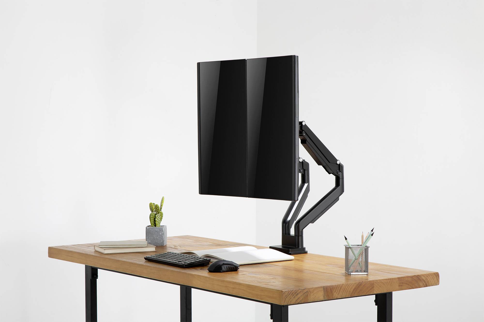 Bild eines aufgeräumten Schreibtischs mit einem Monitorarm, der einen Monitor hält, daneben befinden sich Pflanzen, Tastatur und Maus.